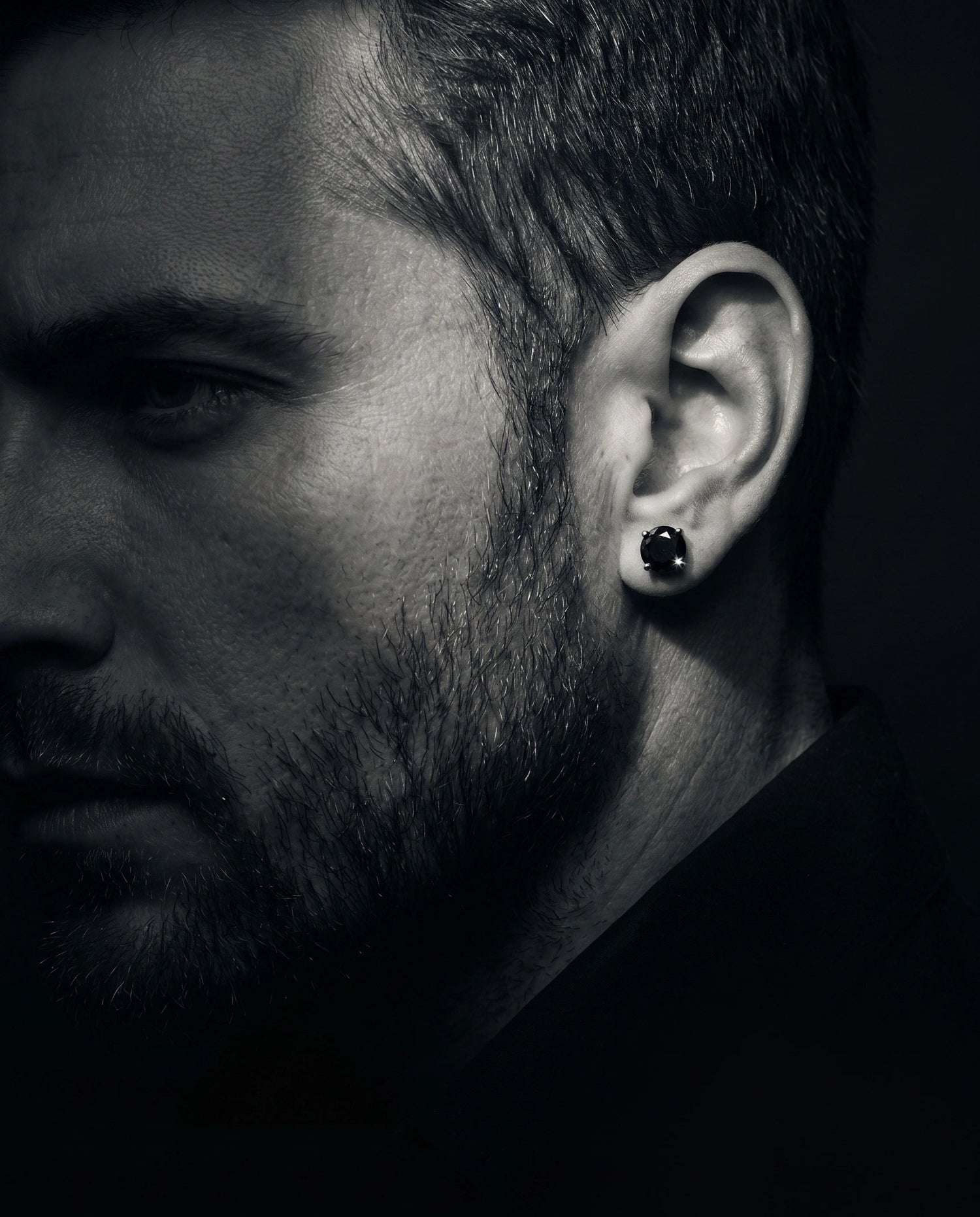 Close-up of a man wearing a black moissanite stud earring against a dark background - Sensitive Stones