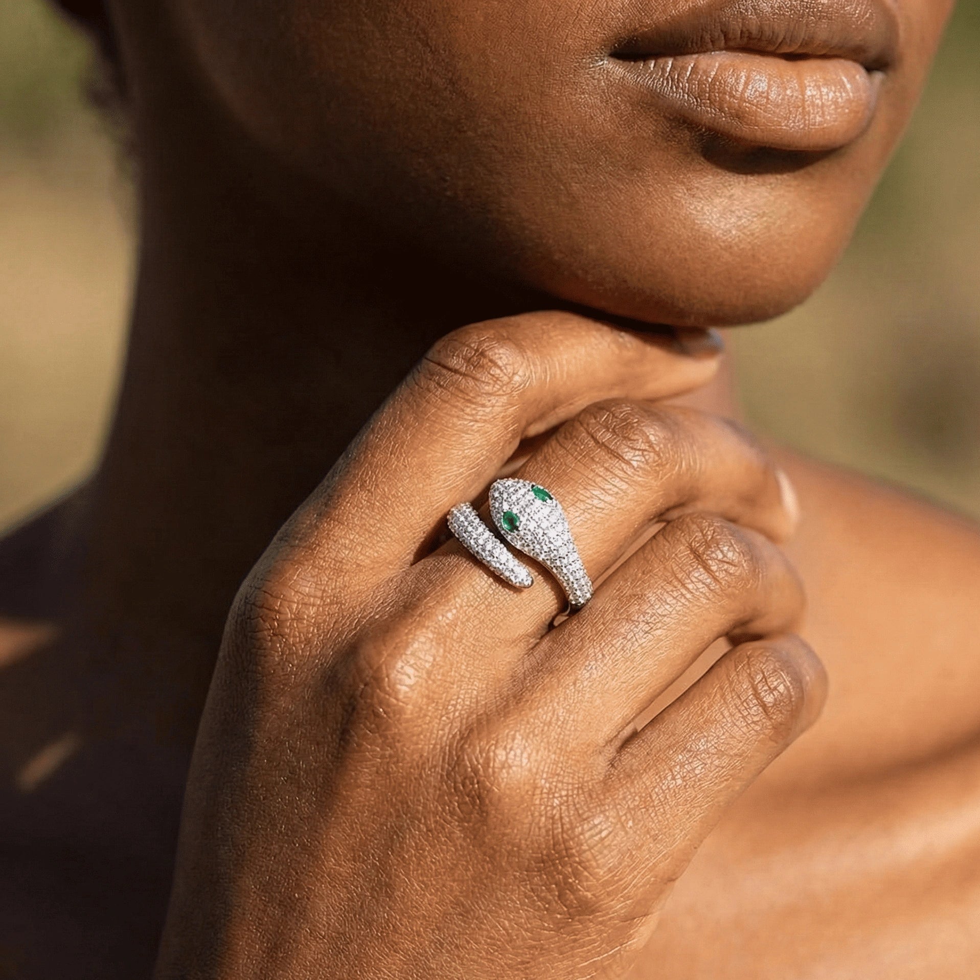 Close-up of a hand wearing a moissanite snake ring in 925 silver with green eye gemstone and featuring dazzling pavé details against a blurred natural background - Sensitive Stones