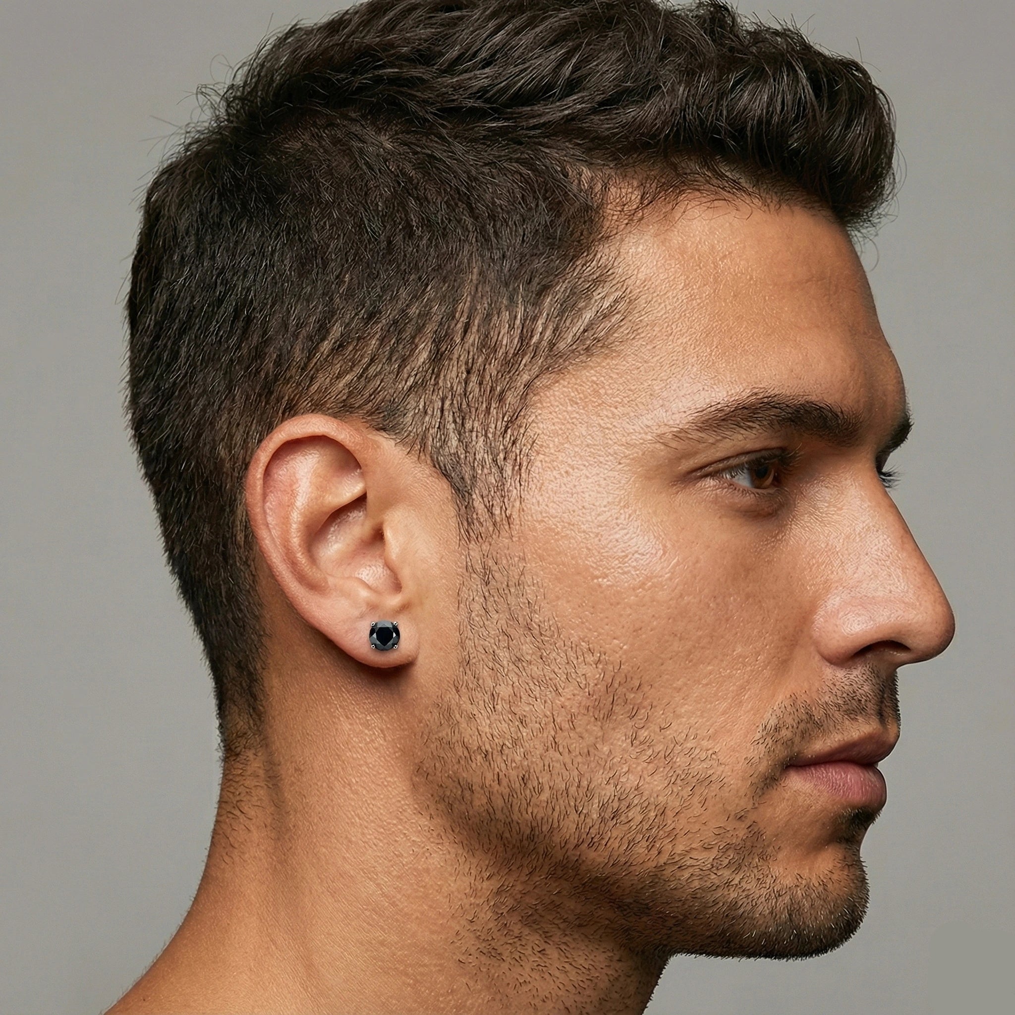 Close-up of a black moissanite stud earring worn on a man's ear, round cut, 4-prong setting - Sensitive Stones