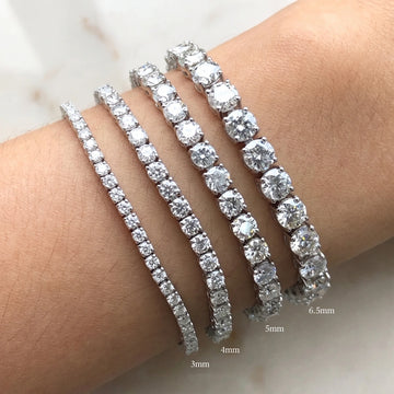 Four moissanite tennis bracelets with clear round-cut stones worn on a wrist, shown with size labels indicating 3mm, 4mm, 5mm, and 6.5mm - Sensitive Stones