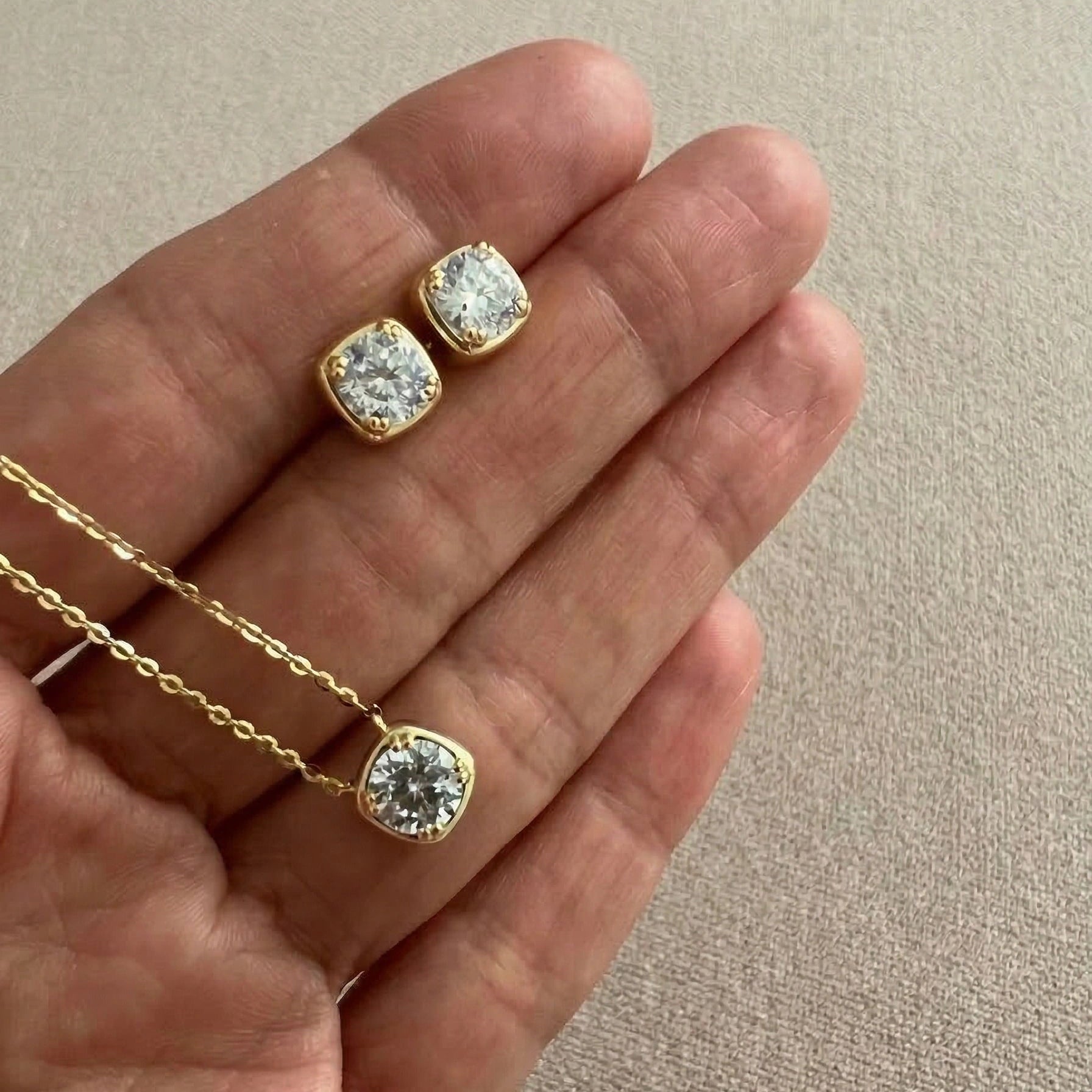 Cushion bezel moissanite necklace and stud earrings set in 18K yellow gold plating held in hand showing size and sparkle - Sensitive Stones