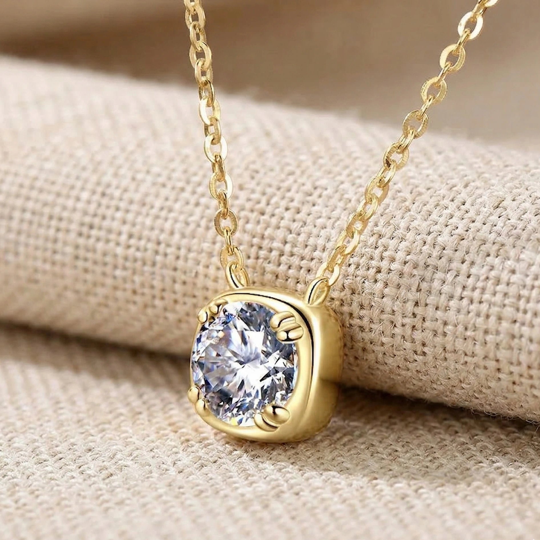 Cushion bezel set moissanite pendant necklace in 18K yellow gold plating resting on linen fabric, close up showing stone detail - Sensitive Stones