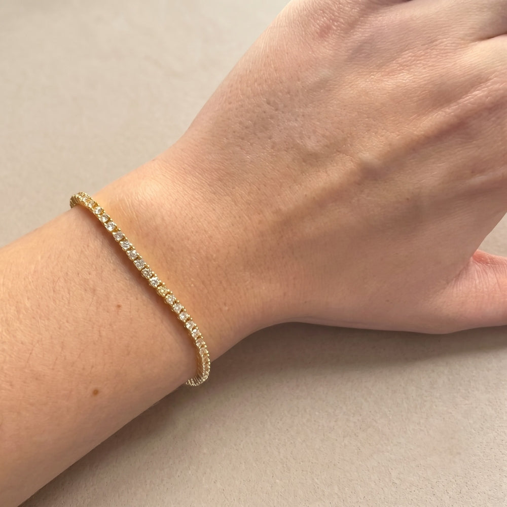 A woman's wrist wearing a dainty yellow gold moissanite tennis bracelet against a soft neutral background - Sensitive Stones