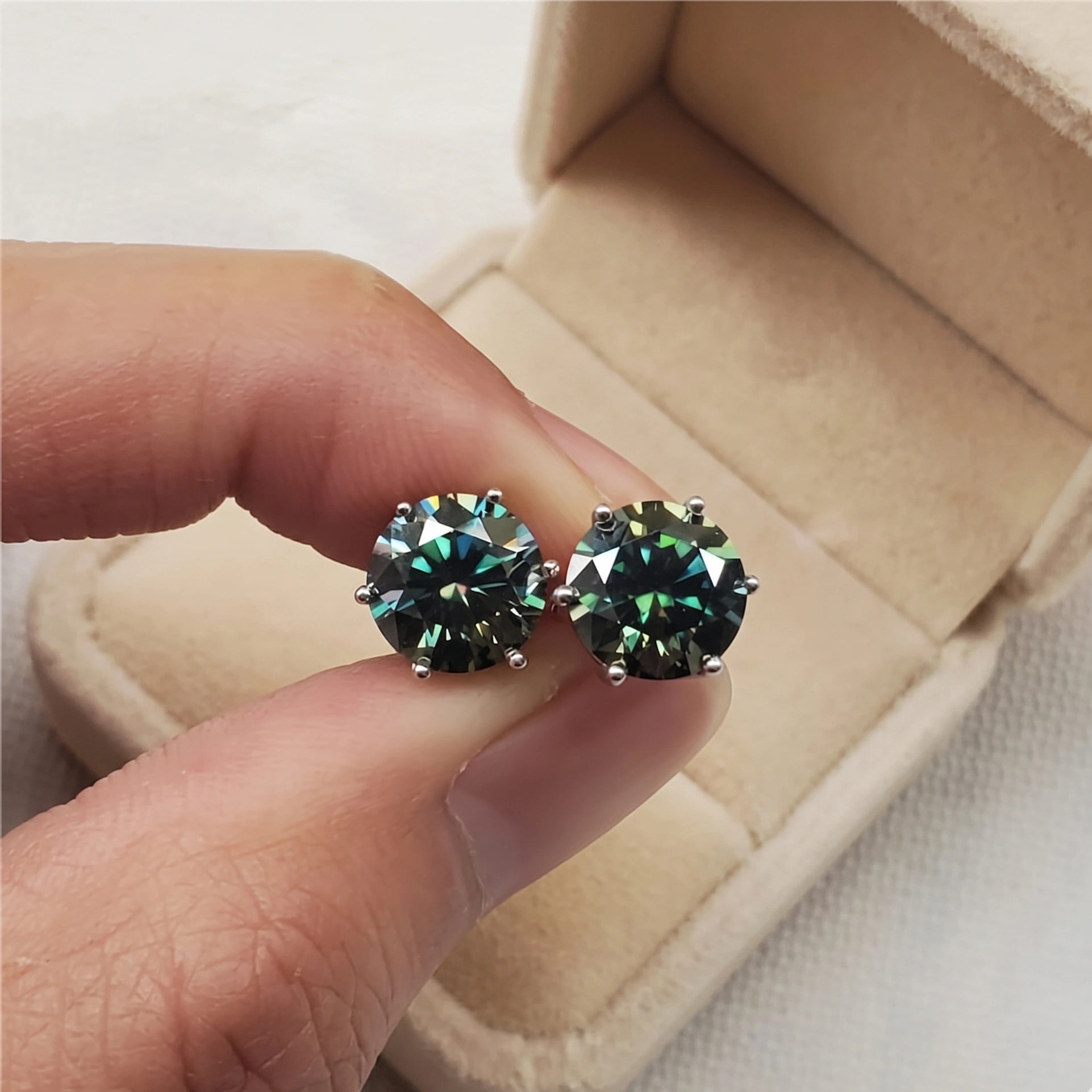 Hand holding dark green moissanite solitaire stud earrings in 6 prong 925 silver setting, close up sparkle - Sensitive Stones