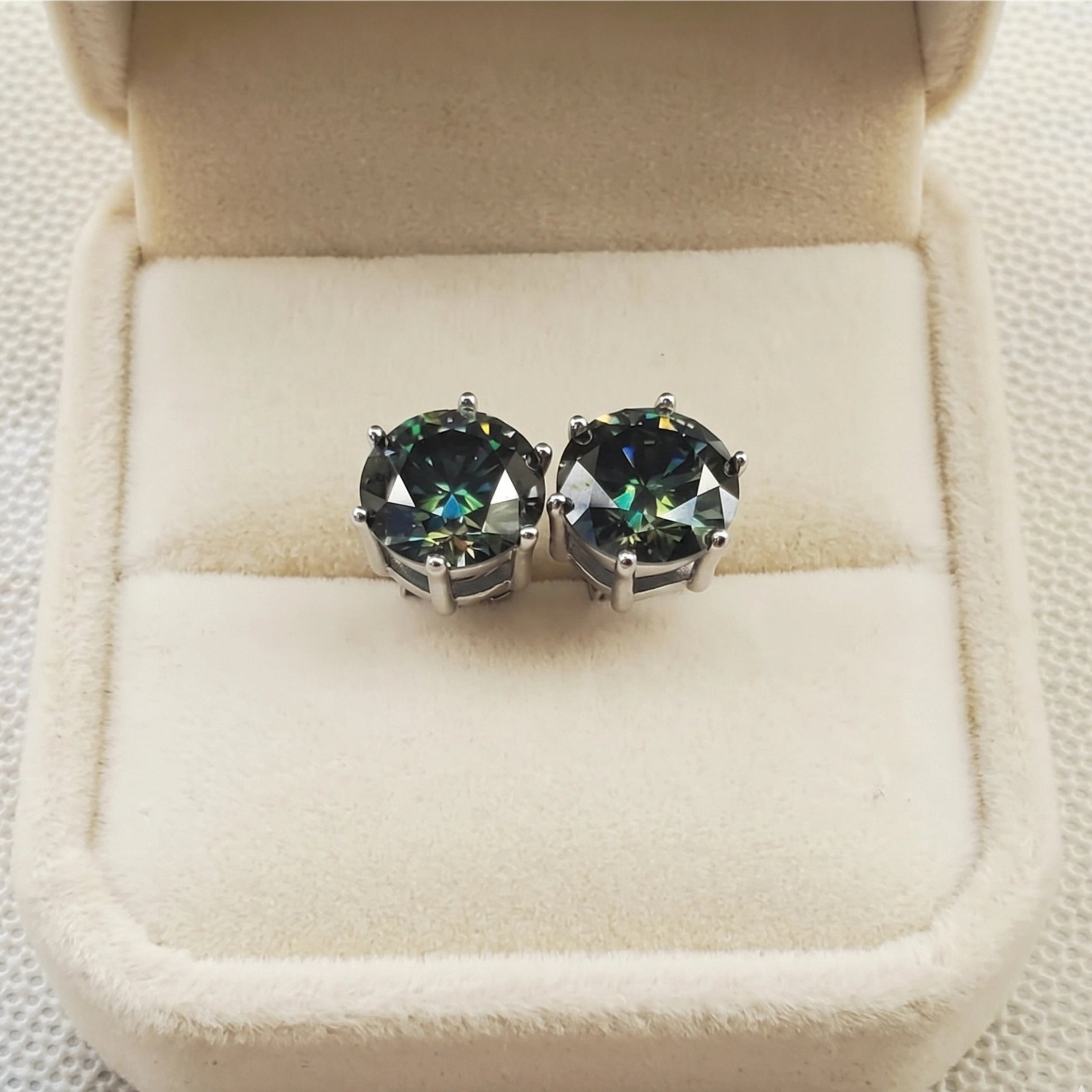 Close up of dark green moissanite solitaire studs in 6 prong 925 silver setting, displayed in soft cream box - Sensitive Stones