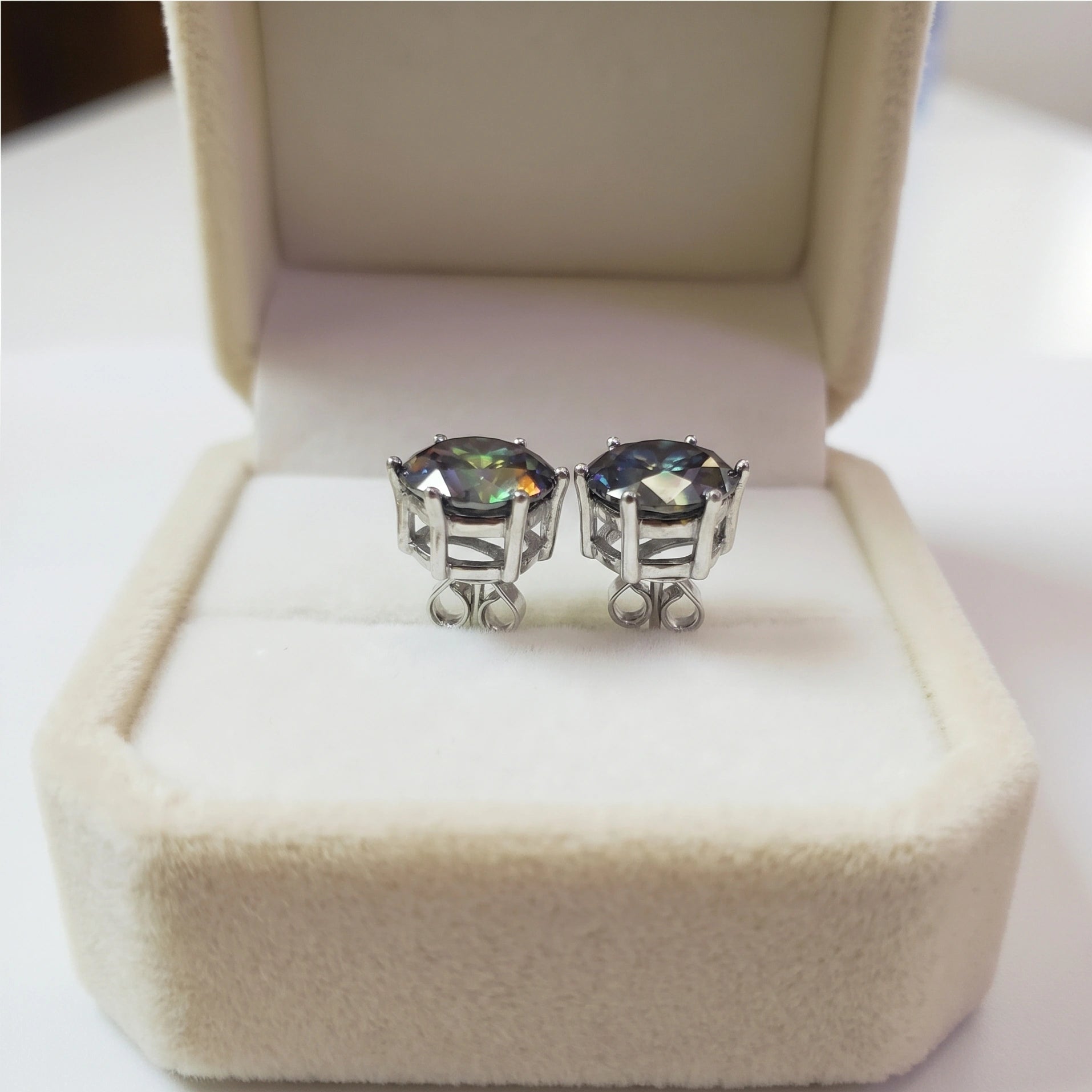 Side profile of dark green moissanite solitaire stud earrings in 6 prong 925 silver setting, displayed in cream jewelry box - Sensitive Stones