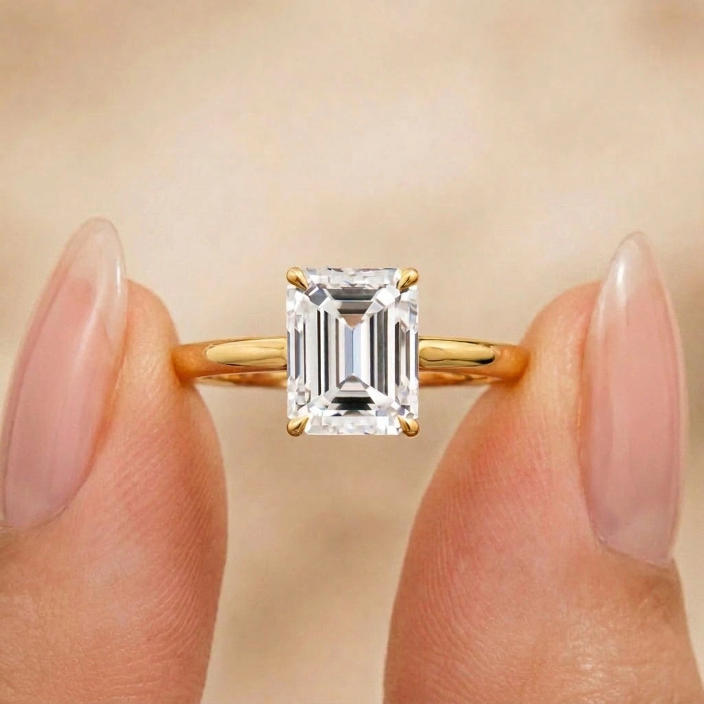 Emerald cut moissanite engagement ring in 14K gold filled held between fingers - Sensitive Stones
