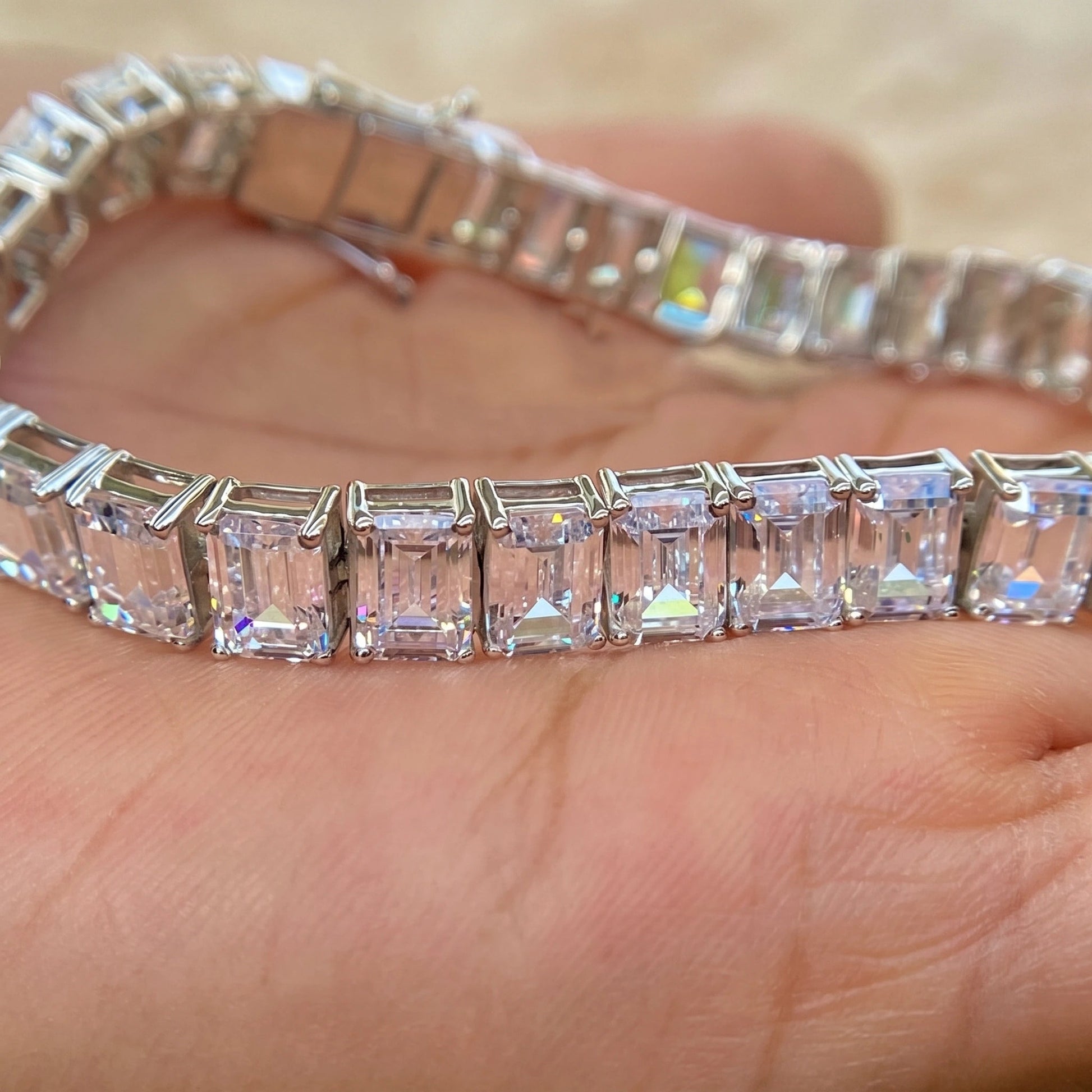 Emerald cut moissanite tennis bracelet held in hand showing the box clasp and step-cut stones in 925 sterling silver - Sensitive Stones