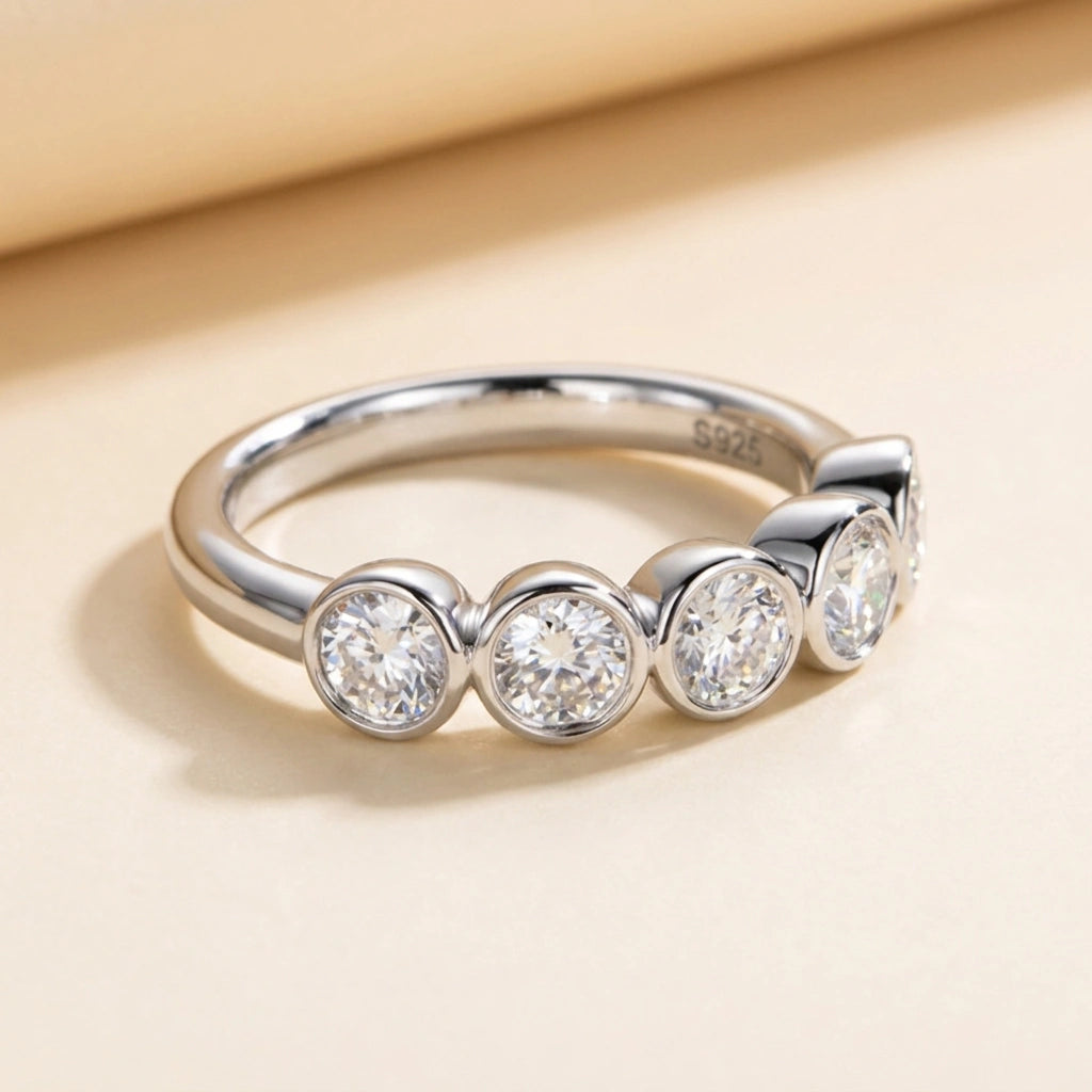 Five stone bezel moissanite ring in rose gold plated 925 sterling silver on a cream surface - Sensitive Stones