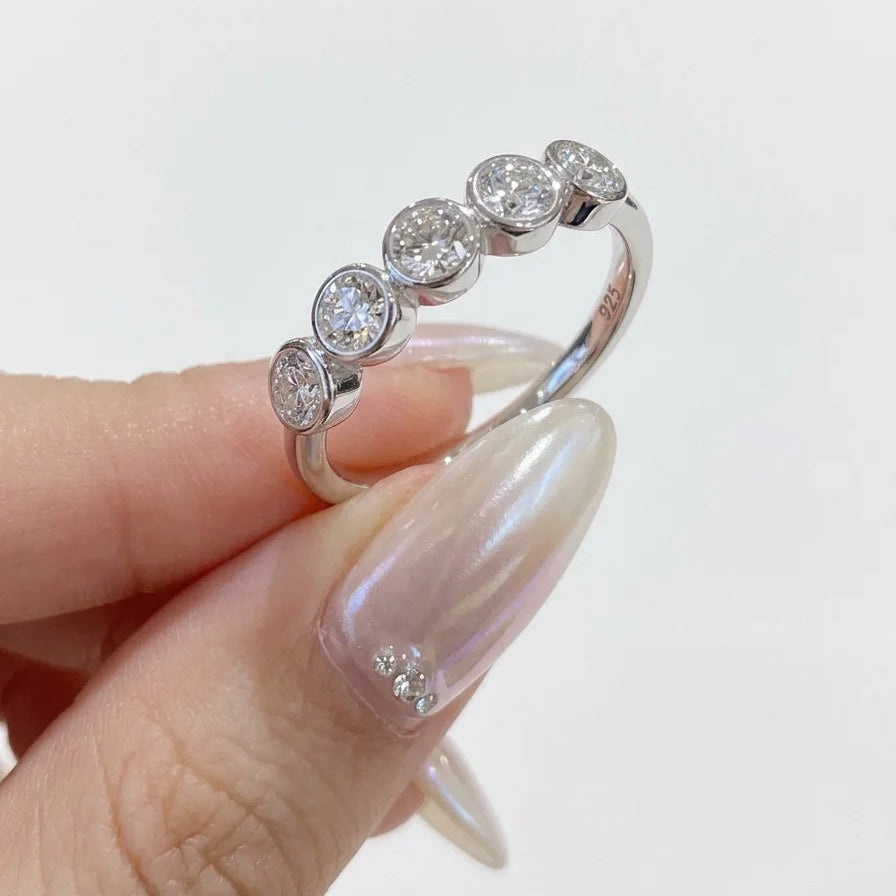Fingers holding the five stone bezel moissanite ring in white gold - Sensitive Stones