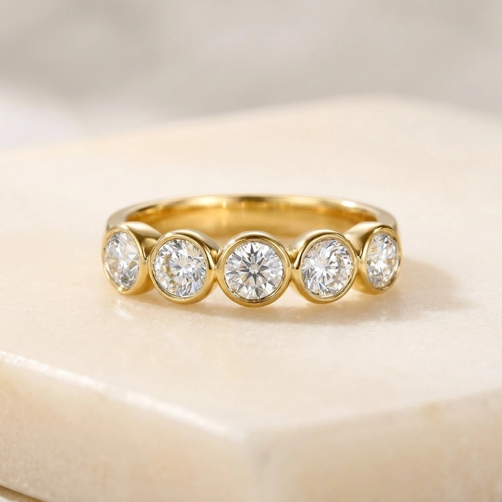 Five stone bezel moissanite ring in yellow gold on a cream stone surface - Sensitive Stones