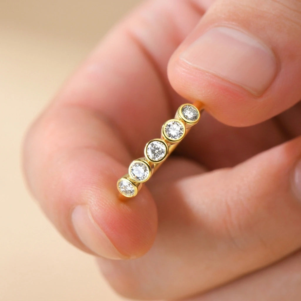 Fingers holding the five stone bezel moissanite ring in yellow gold - Sensitive Stones