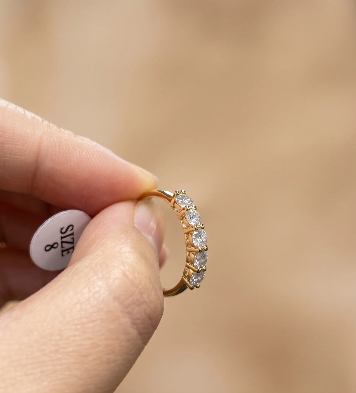 Five stone moissanite stackable ring in 14K gold filled held in hand with a US size 8 tag, showing the slim band profile - Sensitive Stones