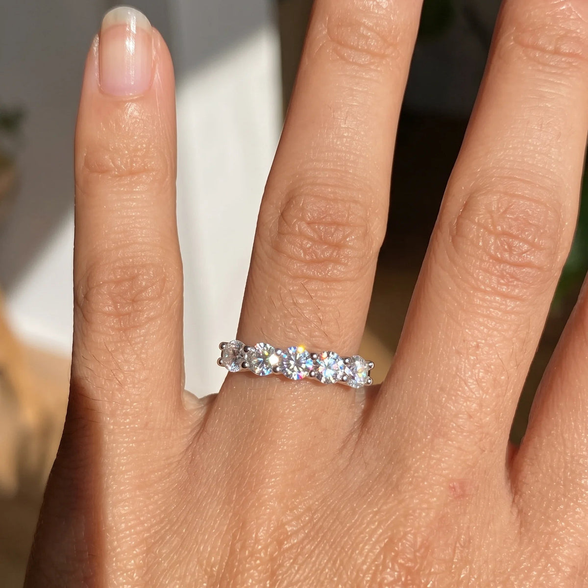 1ct five stone moissanite wedding band in white gold worn on the finger in sunlight - Sensitive Stones