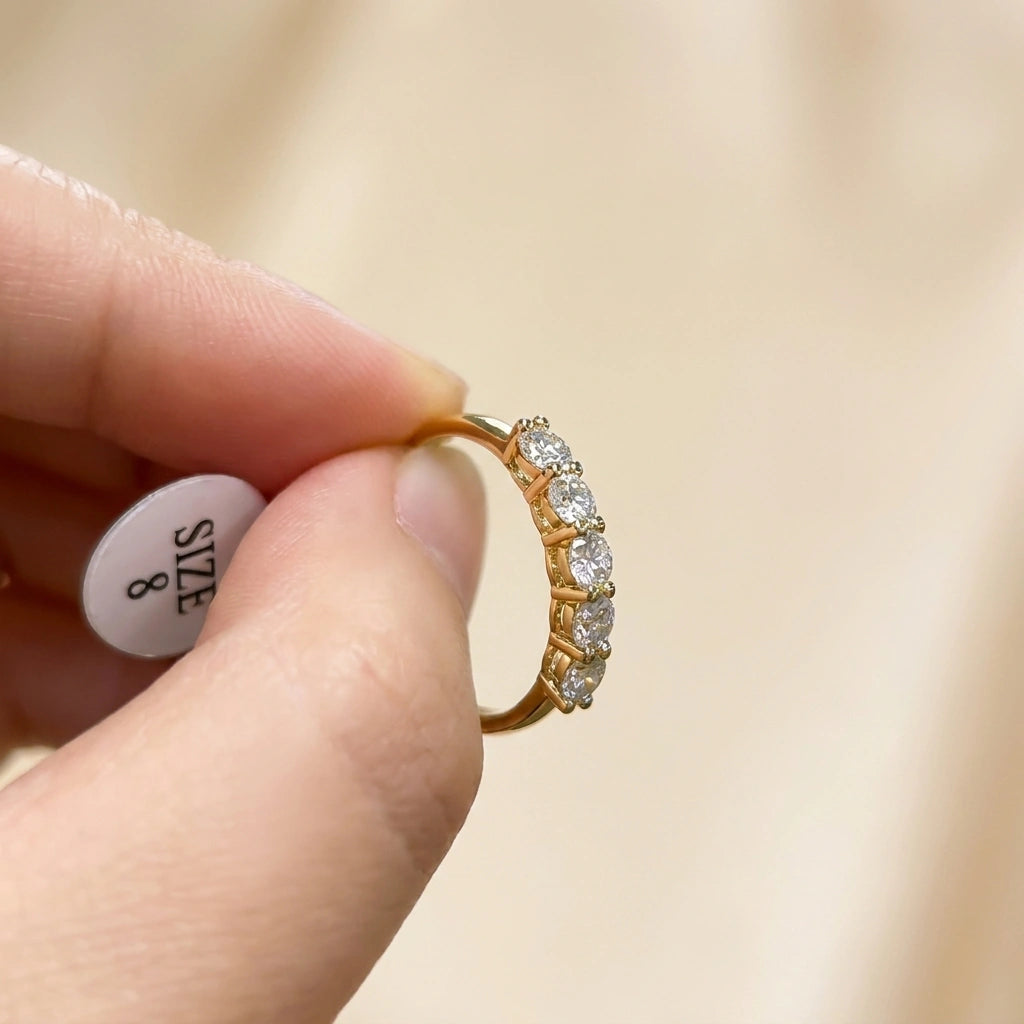 Fingertips holding the five stone moissanite wedding band in yellow gold with size 8 tag - Sensitive Stones