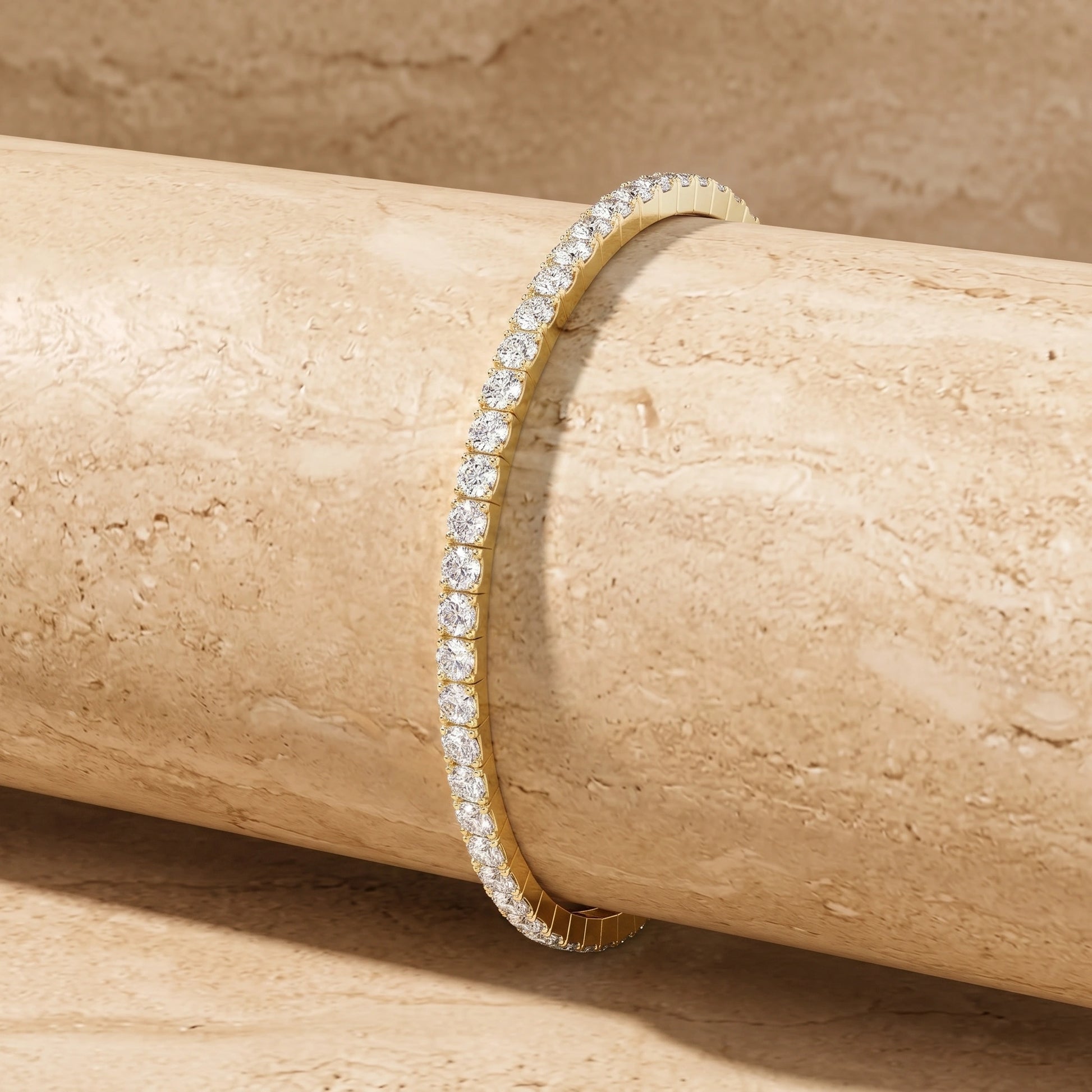 Side view of a 14K gold filled stretch moissanite tennis bracelet draped over a textured beige stone display
