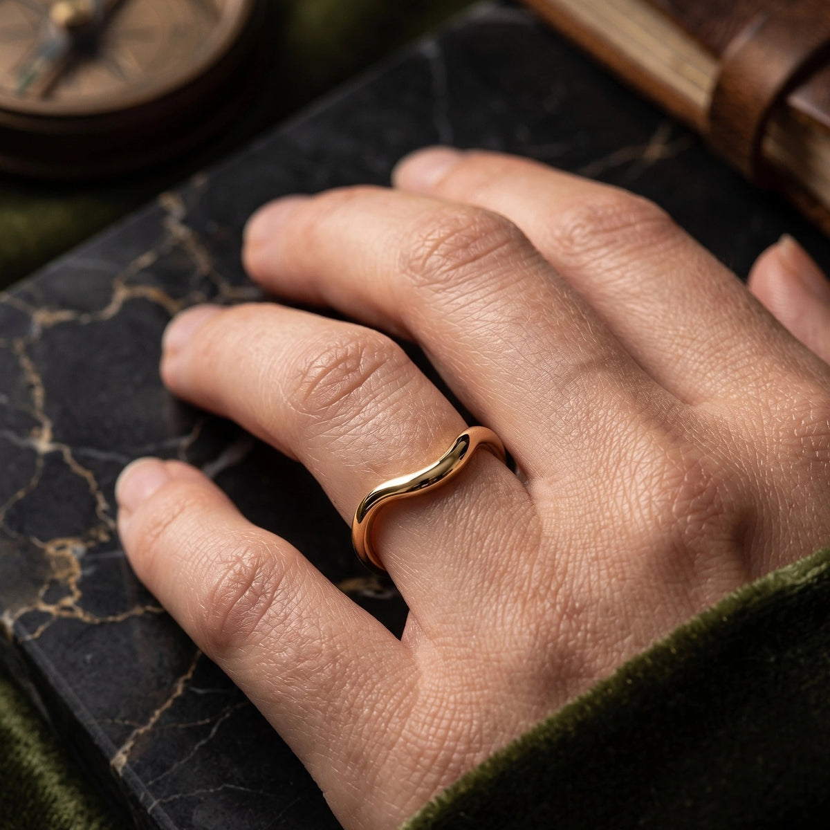 Gold filled curved wedding band worn on hand against a dark leather journal lifestyle shot - Sensitive Stones