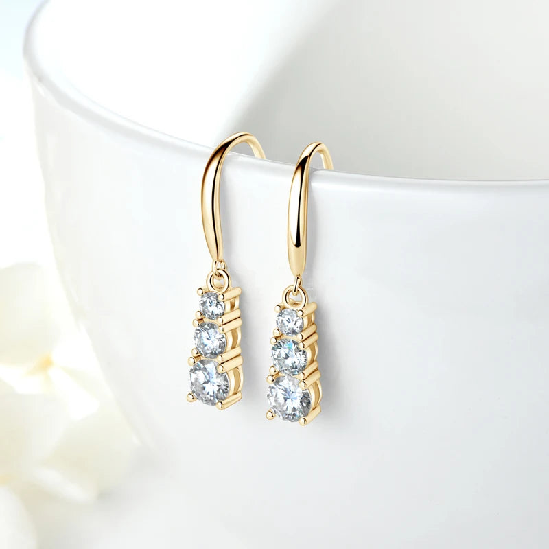 Gold finish moissanite three-stone dangle earrings set in 925 silver displayed on white cup - Sensitive Stones