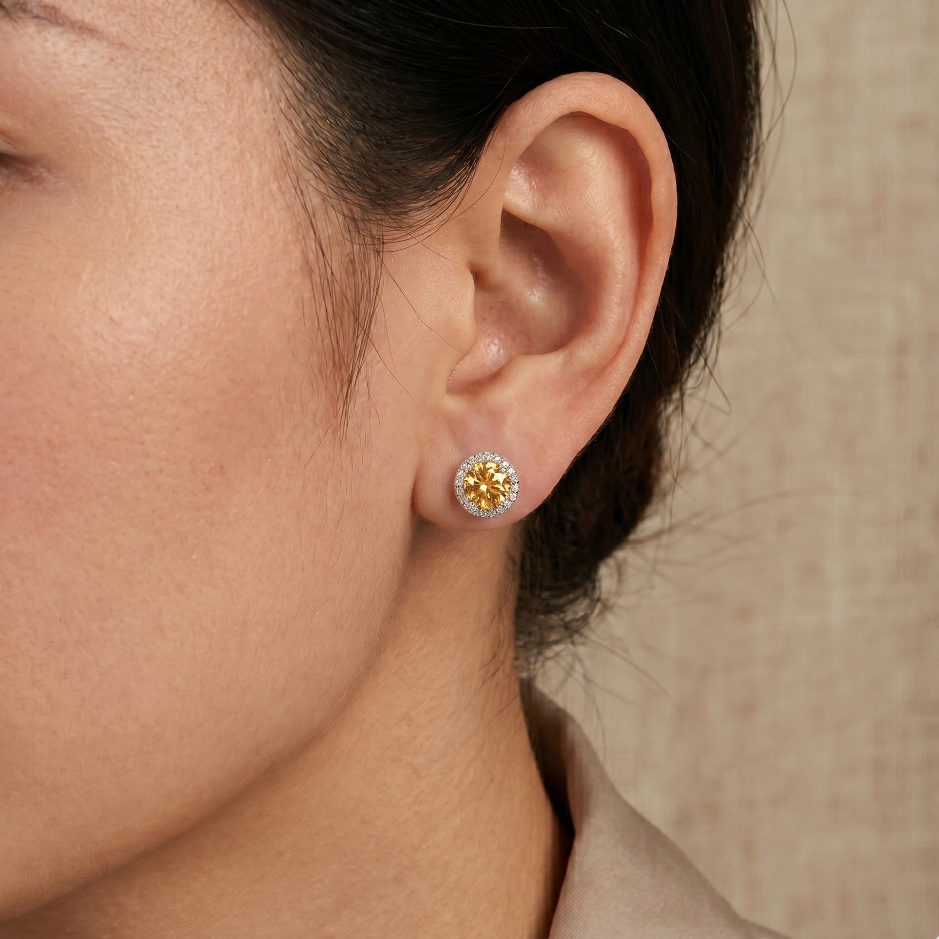Woman wearing 1ct golden yellow moissanite halo stud earrings in 925 sterling silver showing natural size on ear - Sensitive Stones