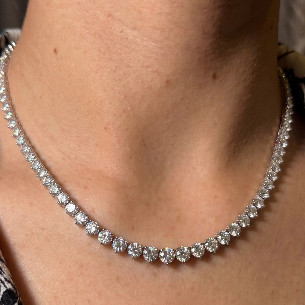 Close-up of a graduated moissanite tennis necklace worn on the neck, showing the three-prong settings and the fire in the stones