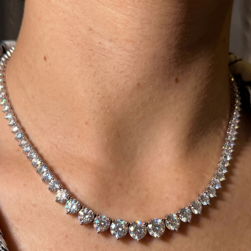 Close-up of a graduated moissanite tennis necklace worn on the neck, showing the three-prong settings and the fire in the stones