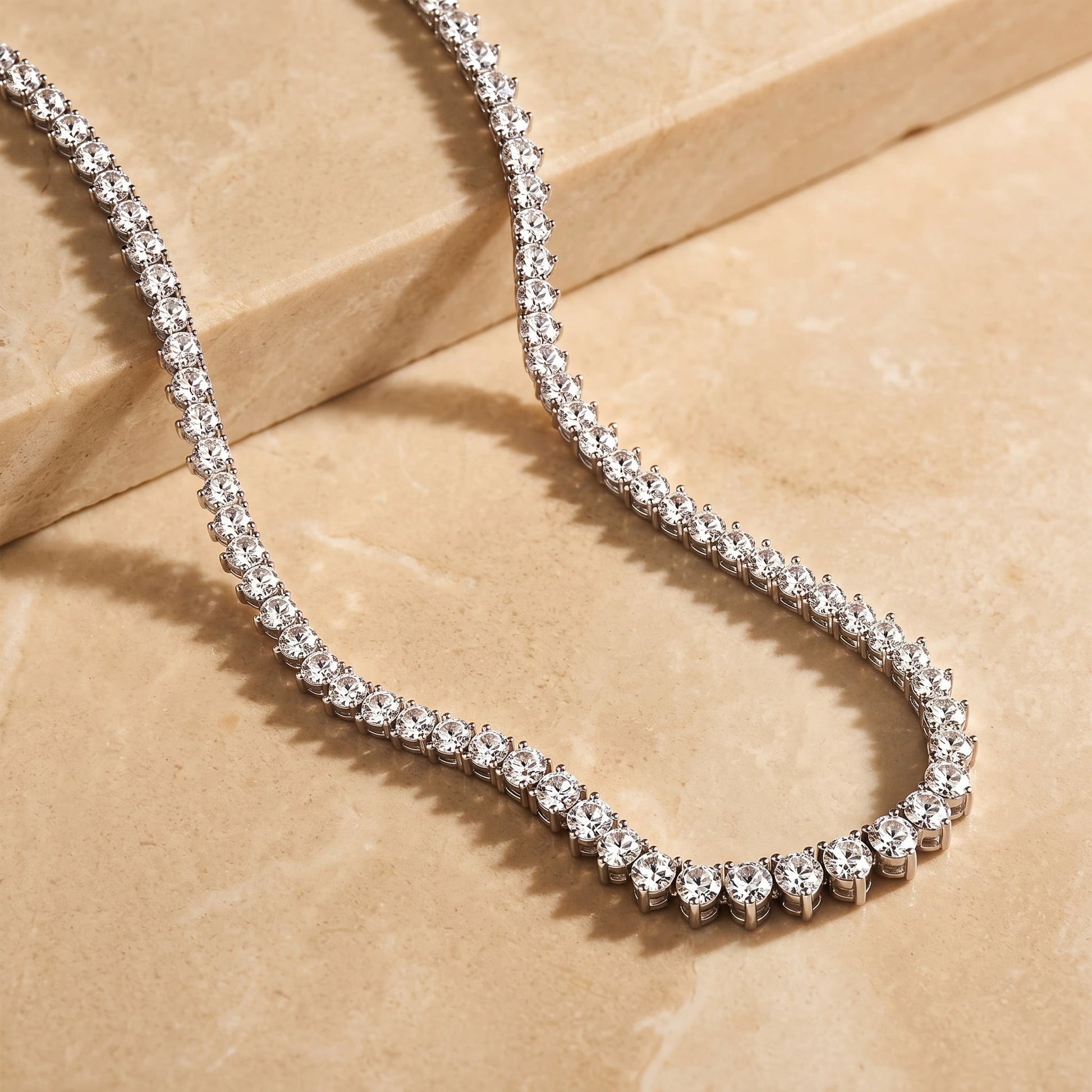 Graduated moissanite tennis necklace laid on stone, smallest stones at the nape rising to the largest at the centre