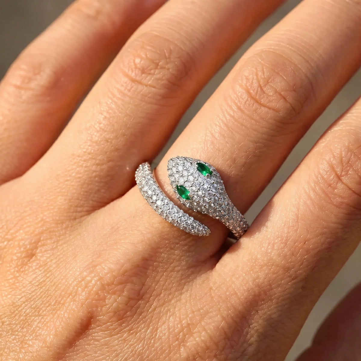 Close-up of a hand wearing the green-eyed moissanite snake ring in a white gold finish in sunlight showing the pave scales and the marquise emerald eyes - Sensitive Stones
