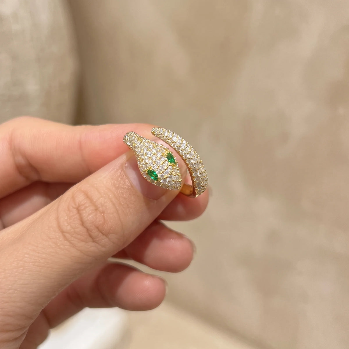 Green-eyed moissanite snake ring in a yellow gold finish held between the fingers showing the open wrap band - Sensitive Stones