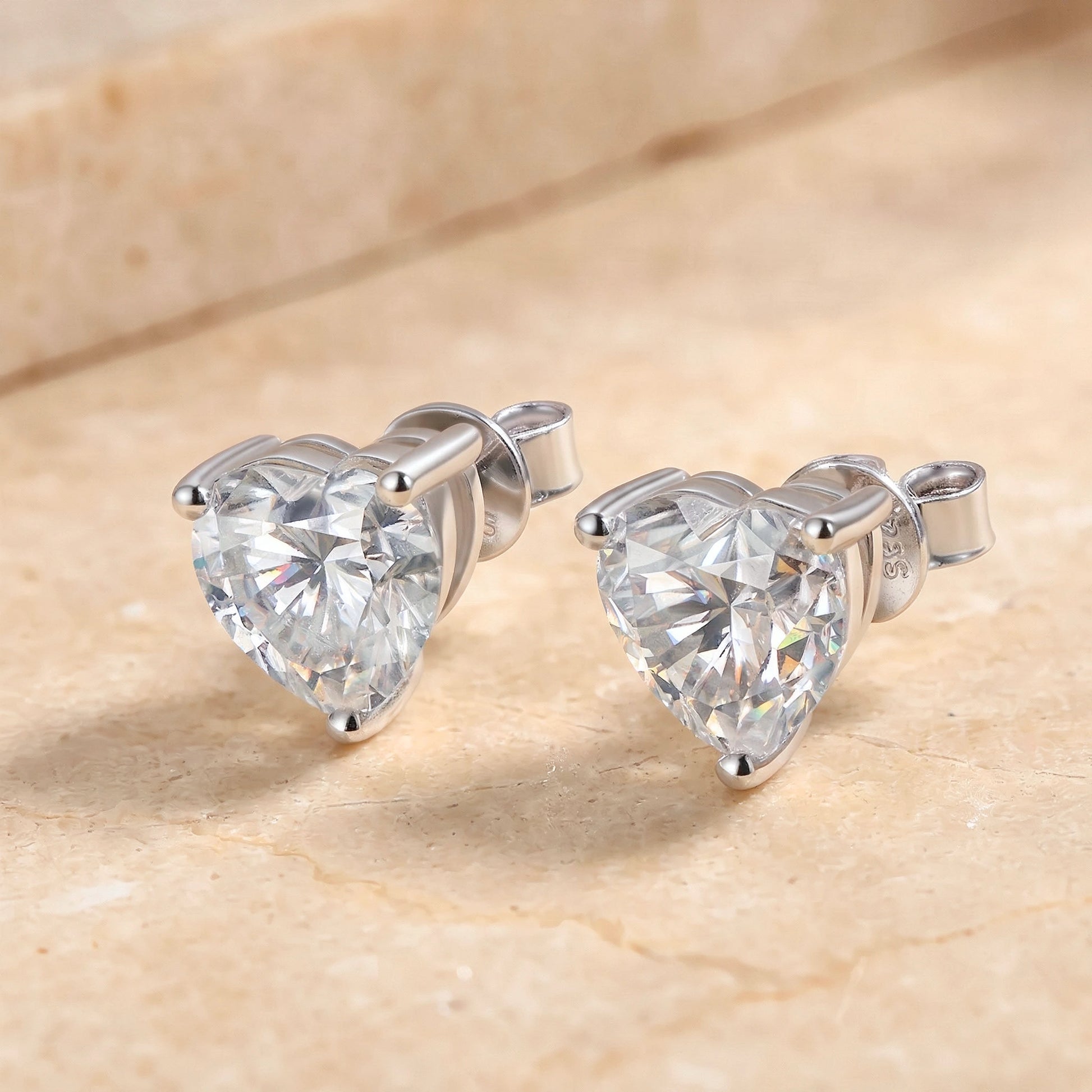 White gold heart cut moissanite stud earrings shown on a stone surface - Sensitive Stones