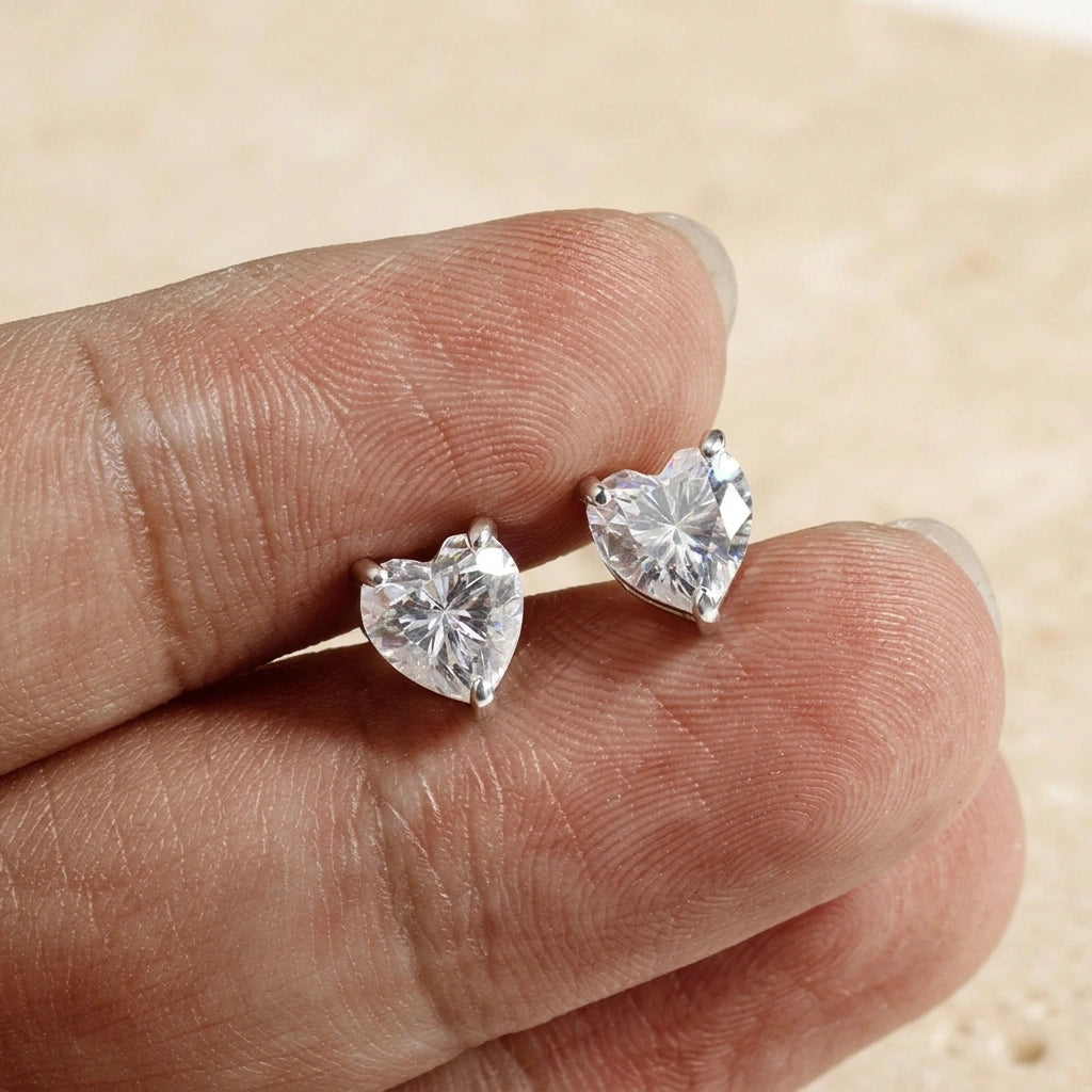 Pair of heart cut moissanite stud earrings in white gold held between fingertips - Sensitive Stones