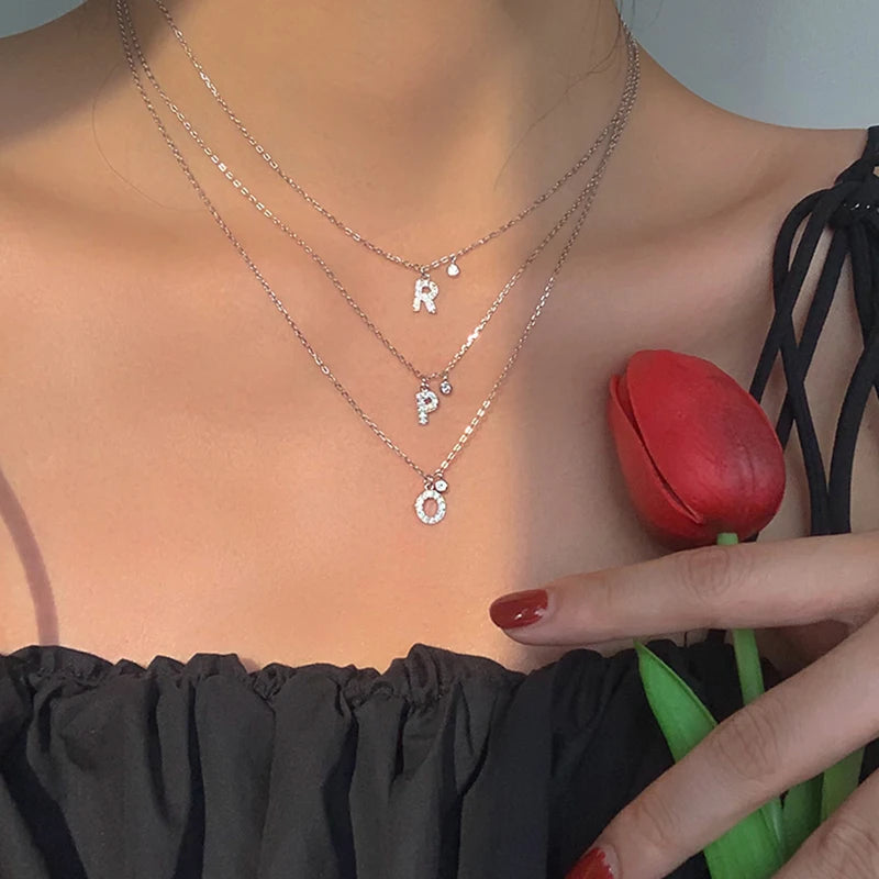 Layered sterling silver initial necklaces with zirconia charms worn with a black off-shoulder top and red tulip.