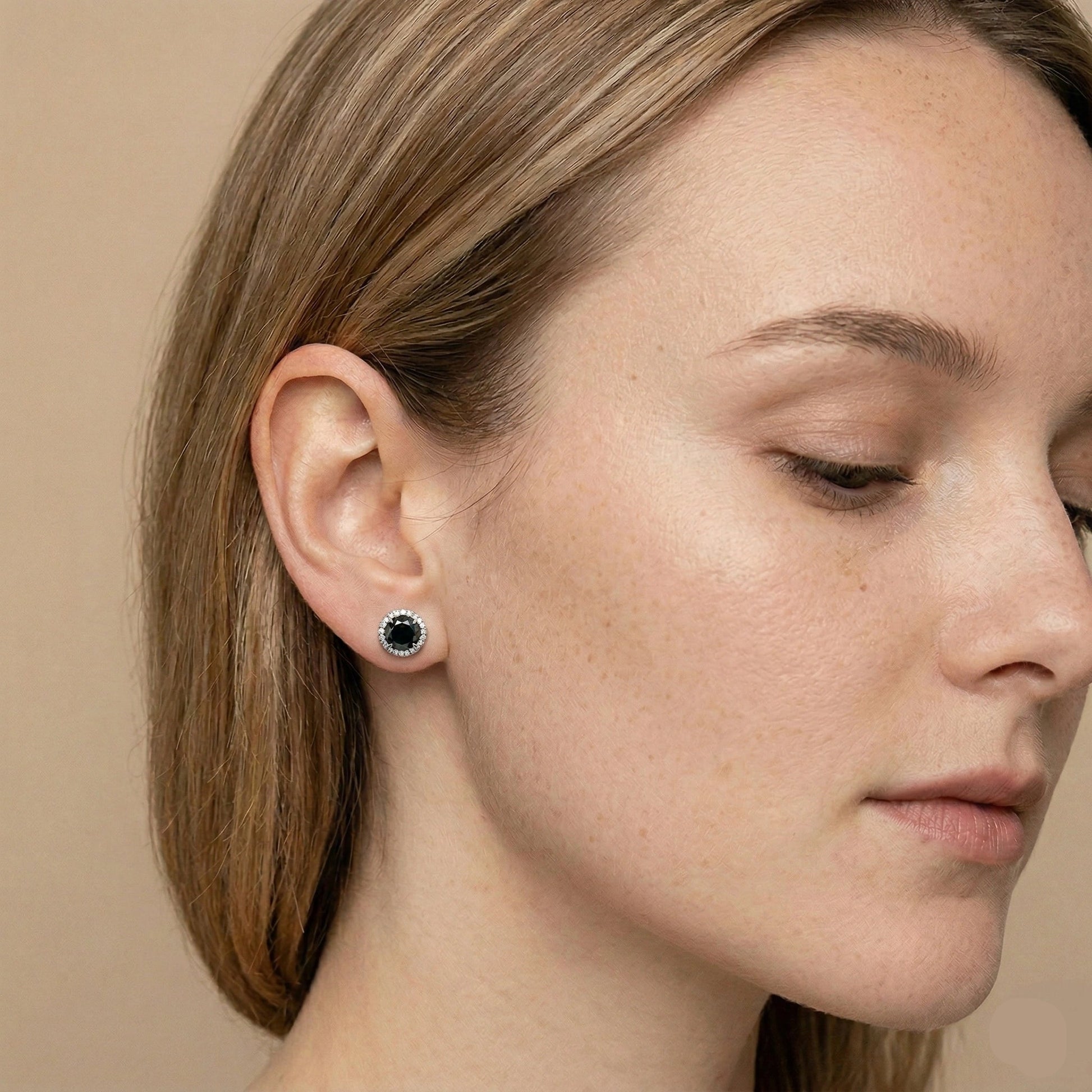 Close-up of 0.8ct black moissanite halo stud earring on ear, round black center with sparkling white halo stones in white gold plated sterling silver - Sensitive Stones