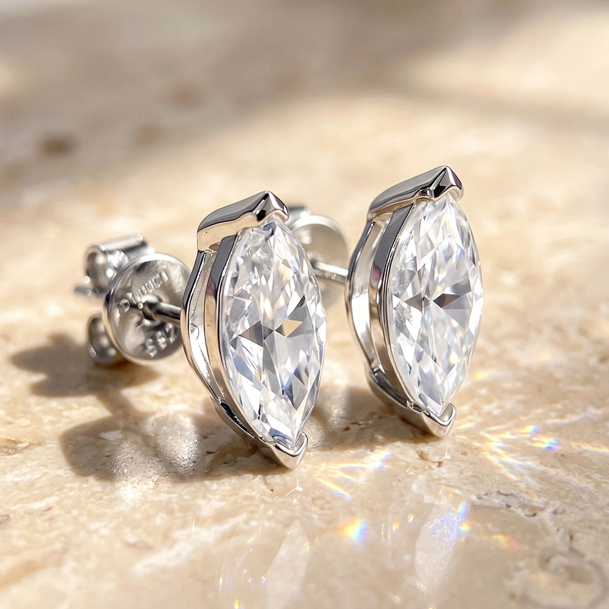 Close-up pair of white gold marquise cut moissanite studs on stone, with a V-prong capping each point and butterfly backs
