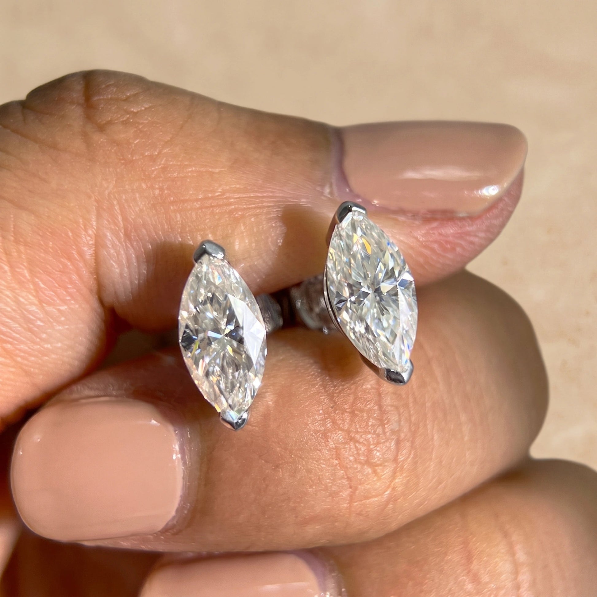 Pair of white gold marquise cut moissanite studs held in the hand to show scale