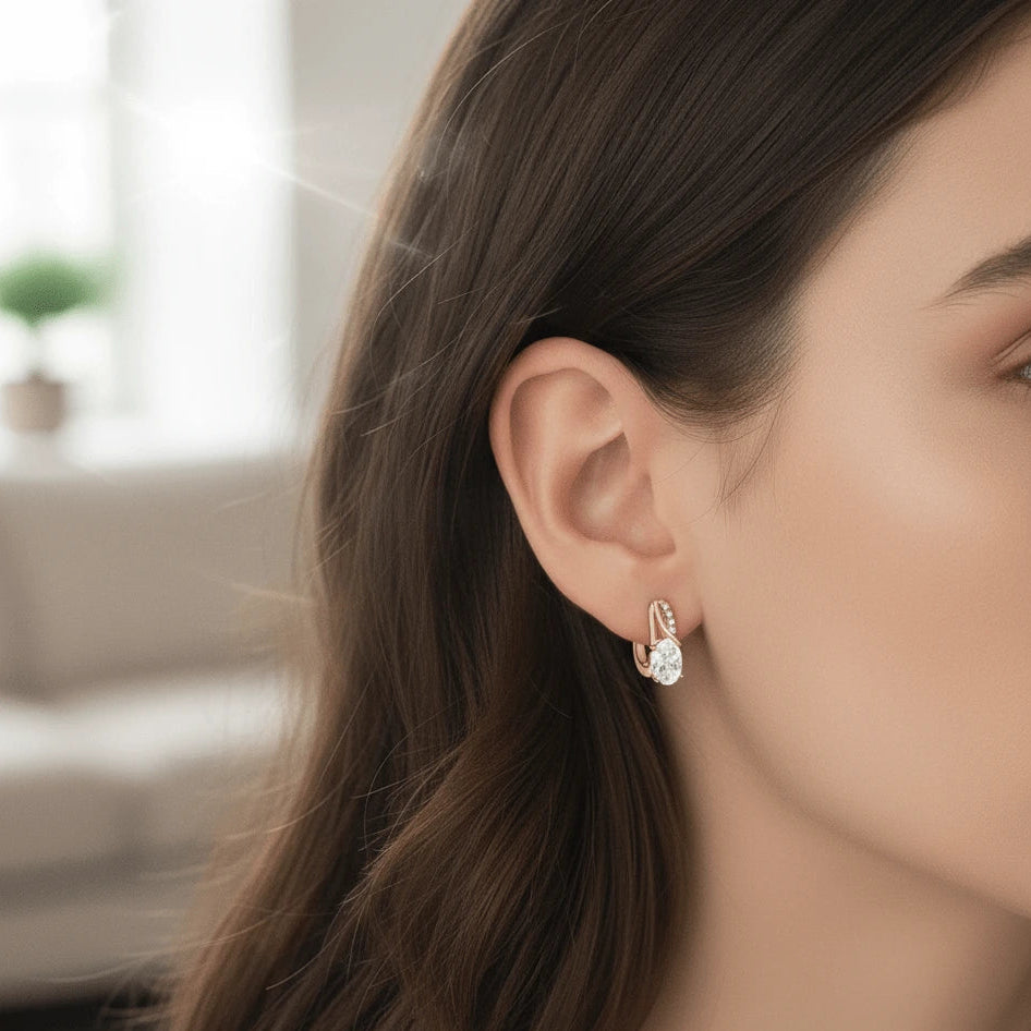 Model wearing 3CT oval moissanite huggie hoop earrings with cubic zirconia accents, side profile close-up showcasing sparkling oval center stone and elegant gold setting - Sensitive Stones