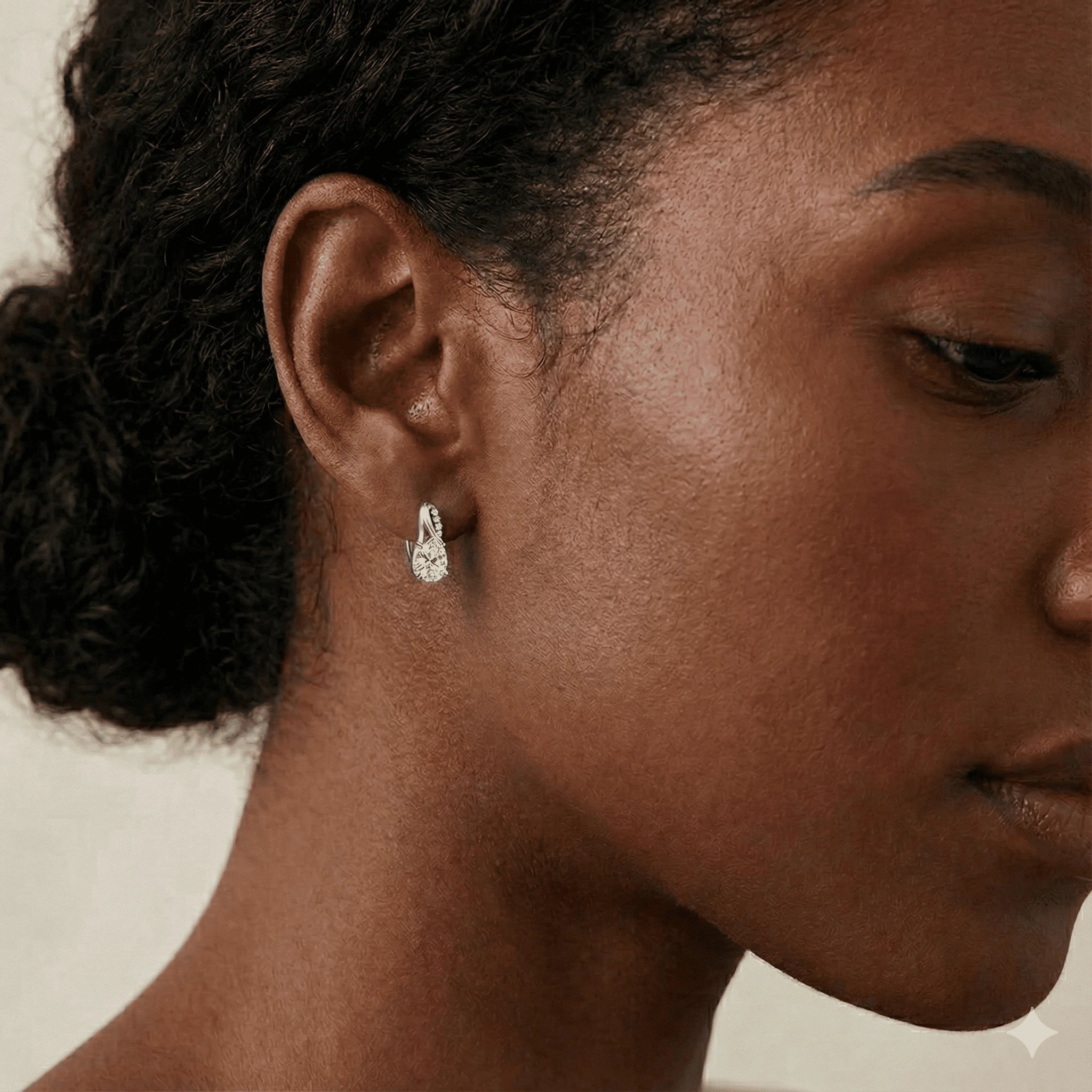 Model wearing 3CT oval moissanite huggie hoop earrings with cubic zirconia accents, side profile close-up showcasing sparkling oval center stone and elegant white gold finish - Sensitive Stones