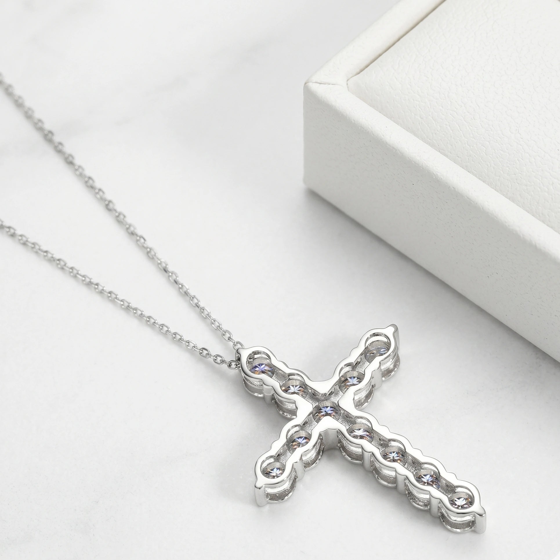 Back view of moissanite cross pendant necklace showing 925 sterling silver prong setting and chain, displayed next to white jewelry box - Sensitive Stones