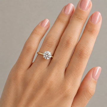 14K gold filled moissanite solitaire engagement ring set in 4-prong worn on model hand resting on marble surface - Sensitive Stones