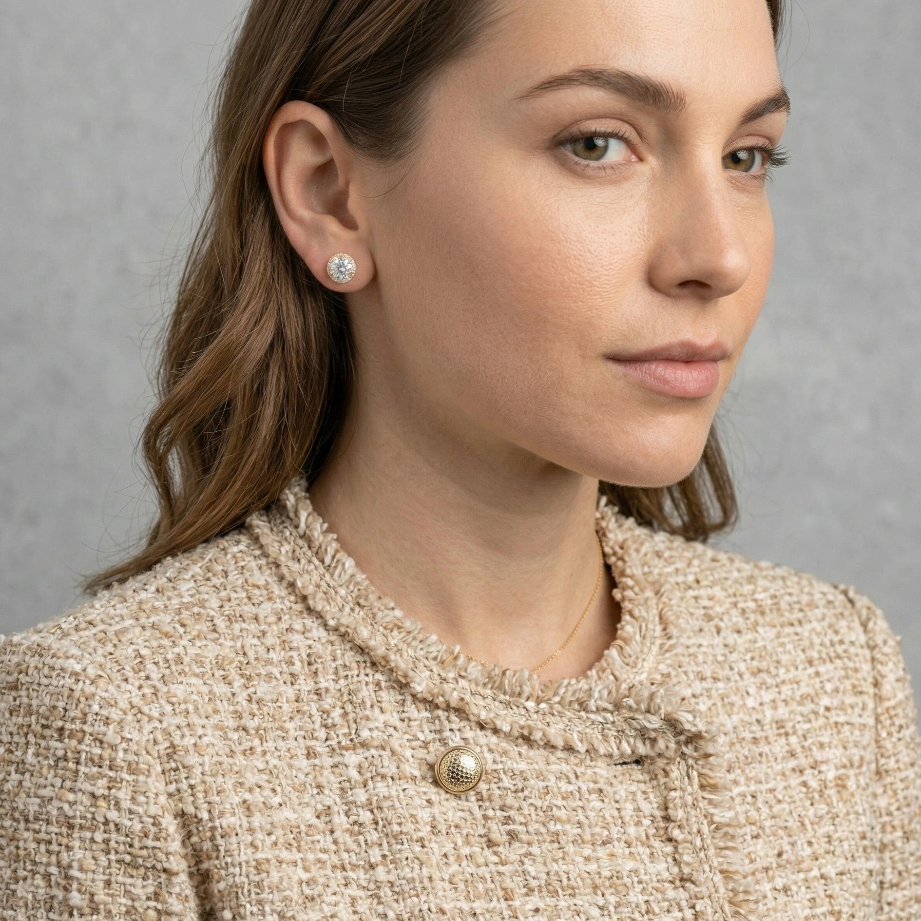 Woman wearing 1ct yellow gold moissanite halo stud earring with D color VVS1 center stone styled with bouclé tweed jacket and gold chain necklace - Sensitive Stones
