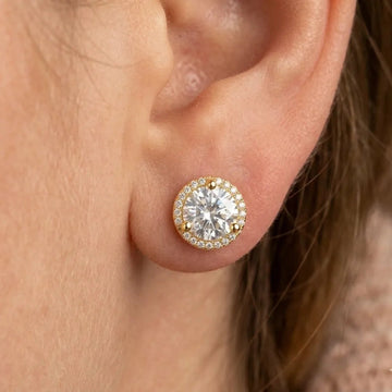  Woman wearing 8mm yellow gold moissanite halo stud earring with full cubic zirconia accent halo on ear - Sensitive Stones