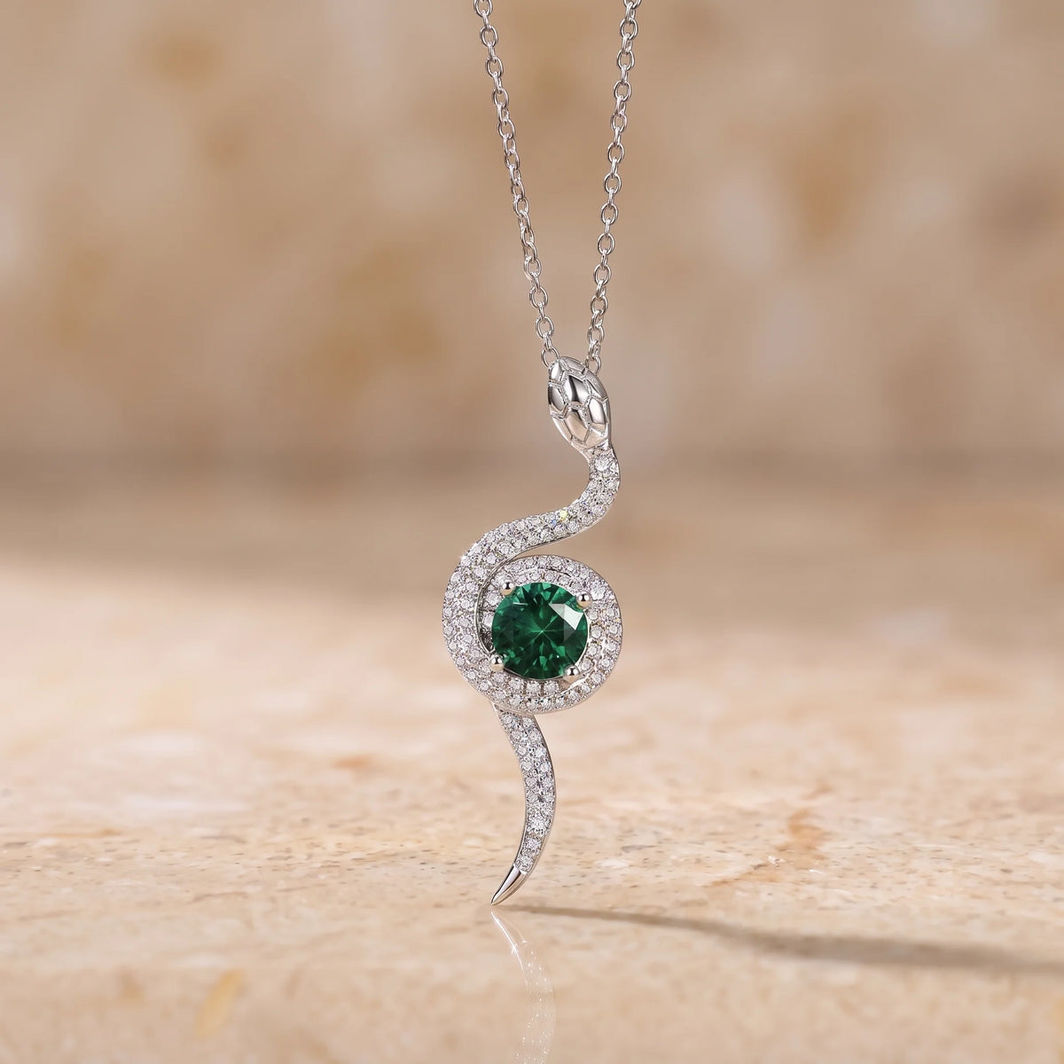 Moissanite serpent's eye pendant necklace in a white gold finish on a stone surface, with a round lab-created emerald center stone - Sensitive Stones
