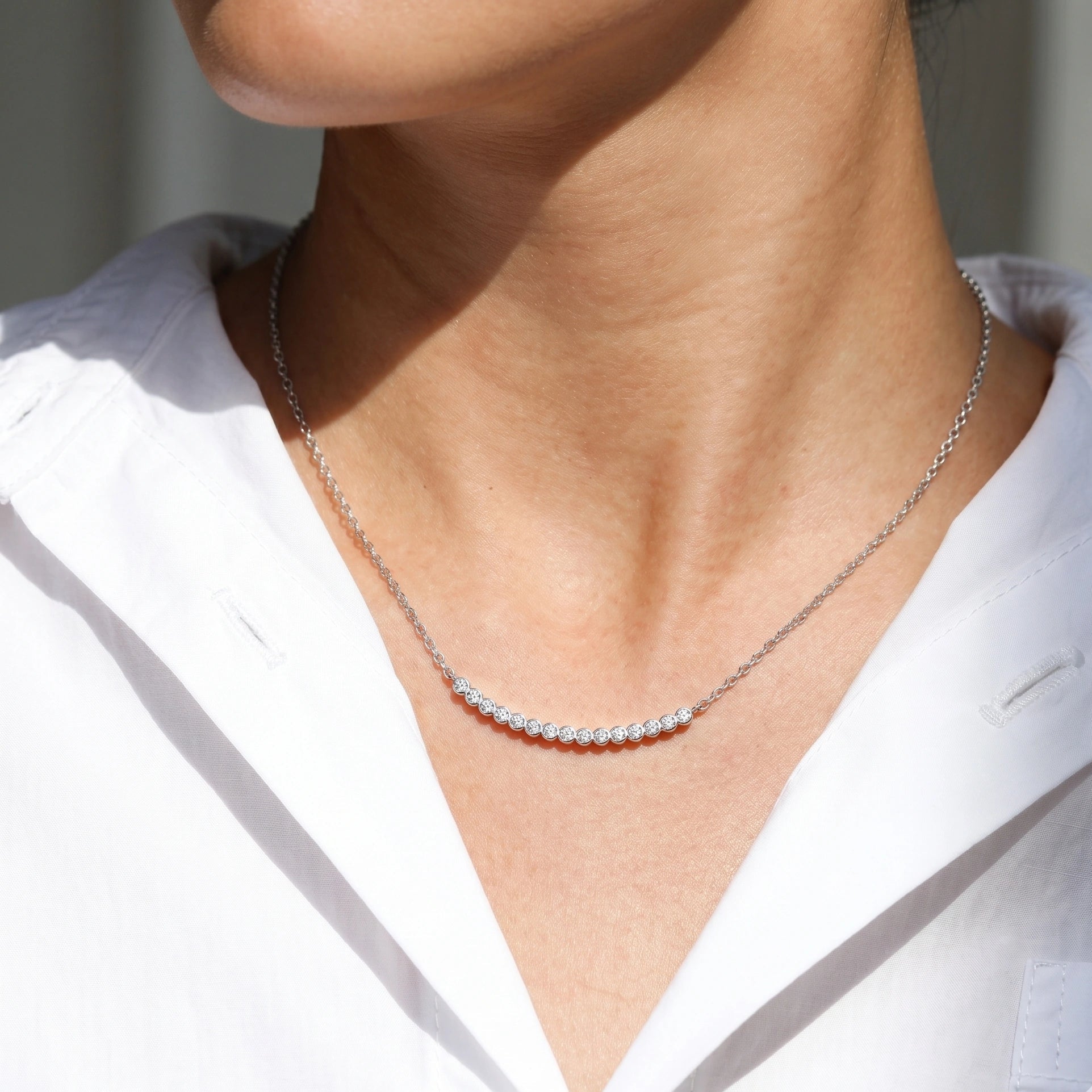 Woman wearing moissanite curved bar necklace in 18K white gold plated 925 silver at collarbone - Sensitive Stones