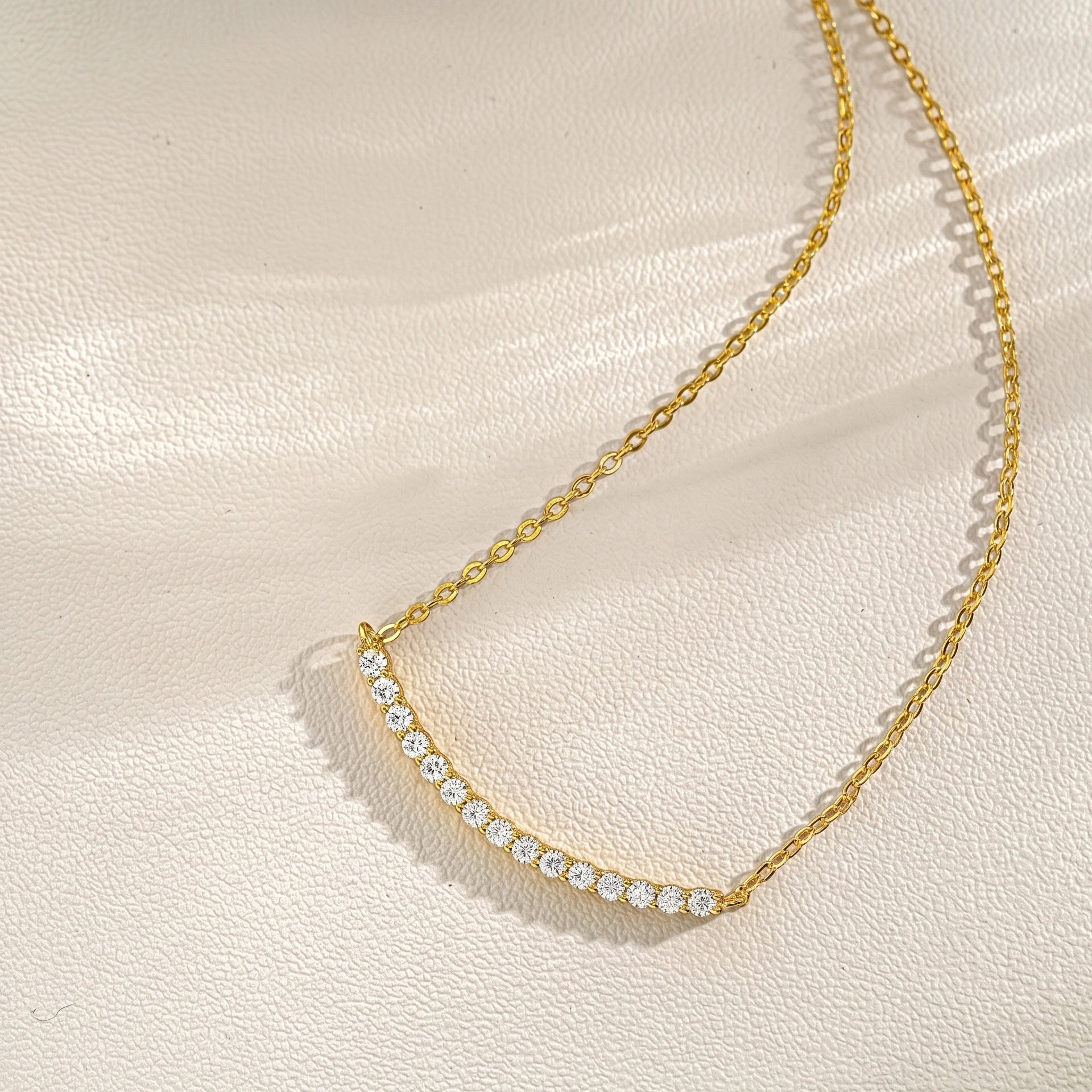 18K yellow gold moissanite smile bar necklace on cream fabric, curved tennis bar design - Sensitive Stones