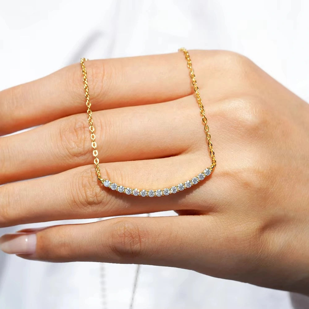 Hand holding moissanite smile bar necklace in yellow gold showing size and stone brilliance - Senstive Stones