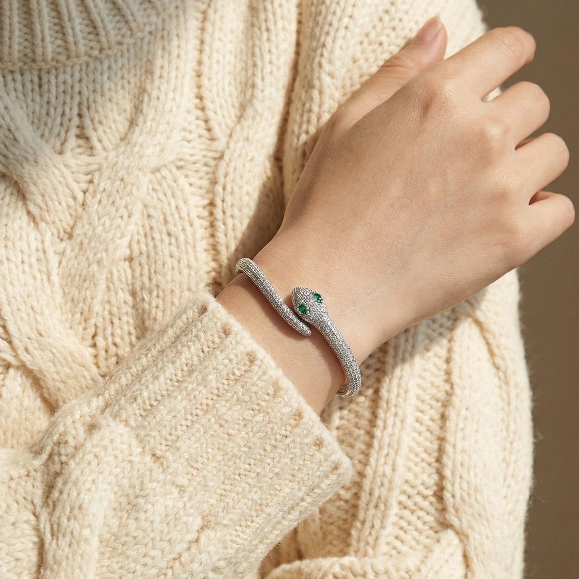 Woman wearing moissanite snake bracelet in 925 silver with green nano gemstones on wrist, styled with cream knit sweater - Sensitive Stones