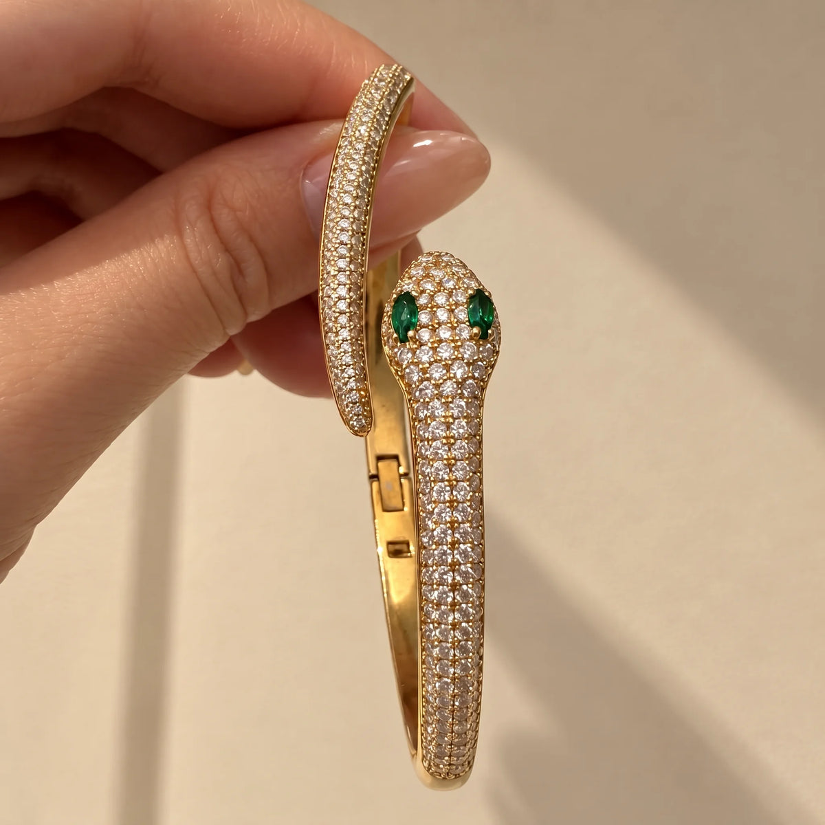 Moissanite snake bracelet in a yellow gold finish held open on its hinge, showing the clasp and the pavé serpent with green lab-created emerald eyes - Sensitive Stones
