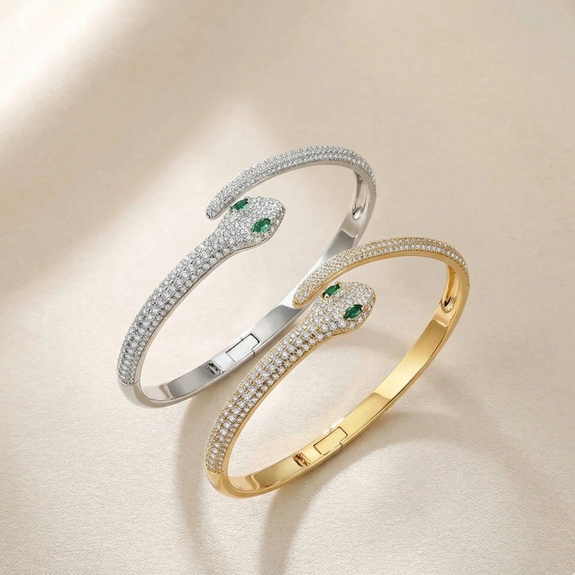 Two moissanite snake bracelets - one in white gold plating and one in yellow gold plating, featuring marquise-cut lab-emerald accent stones and hinged cuff closure - Sensitive Stones