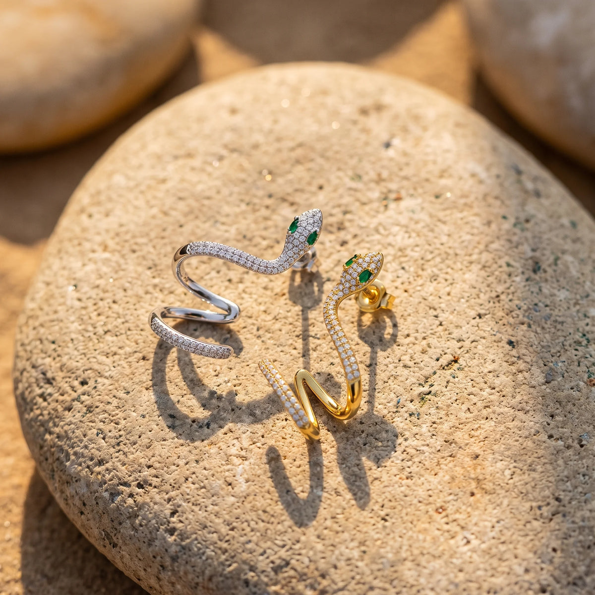 Moissanite snake ear climber earrings in white gold and yellow gold finishes side by side on a stone, showing the butterfly backs behind the snake heads - Sensitive Stones