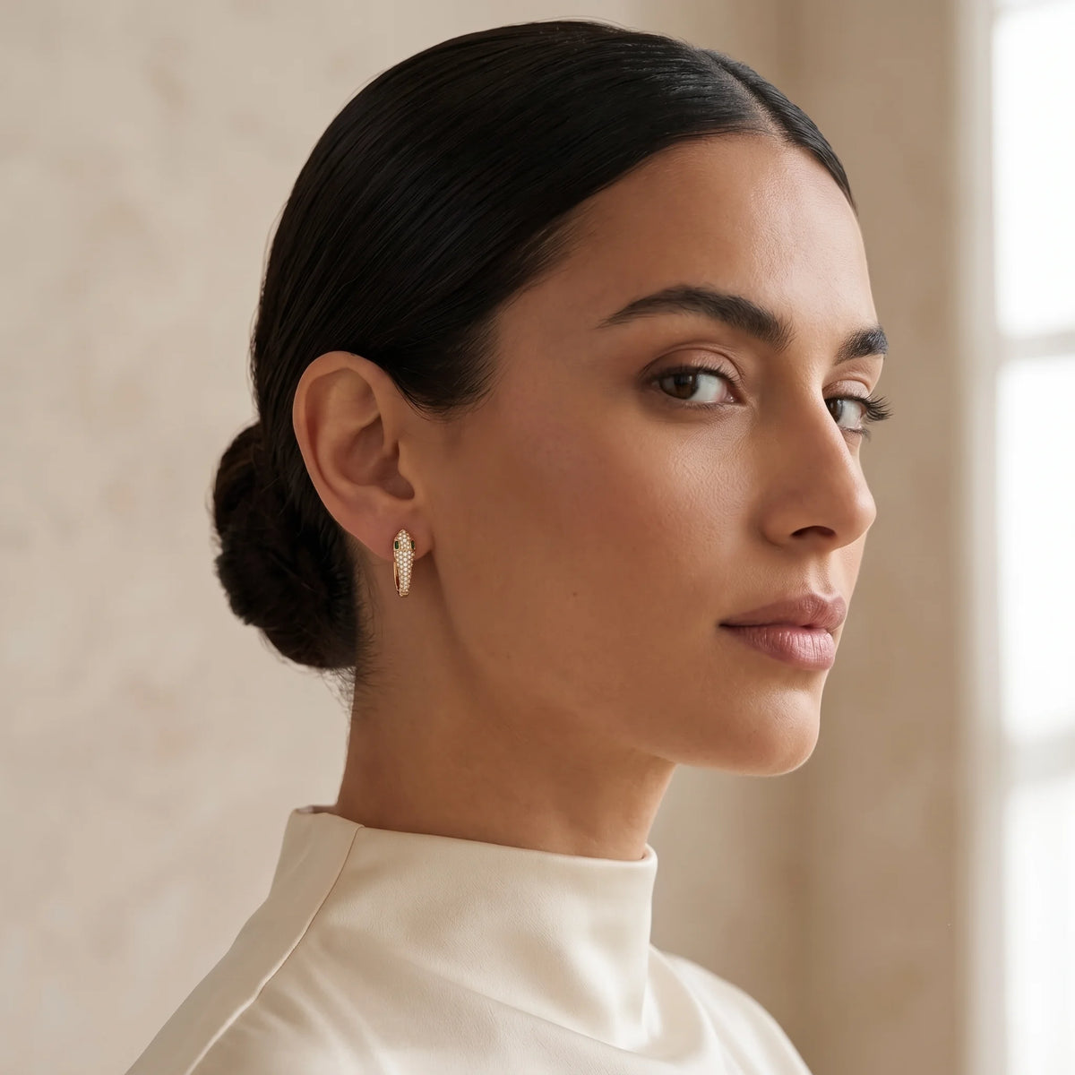 Woman with her hair in a bun wearing the small moissanite snake hoop earrings in a yellow gold finish, showing their subtle size - Sensitive Stones