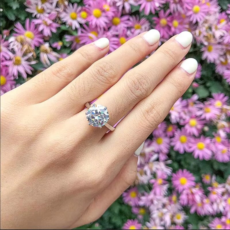 Hand wearing a 4ct silver moissanite solitaire ring with pink flowers in the background - Sensitive Stones